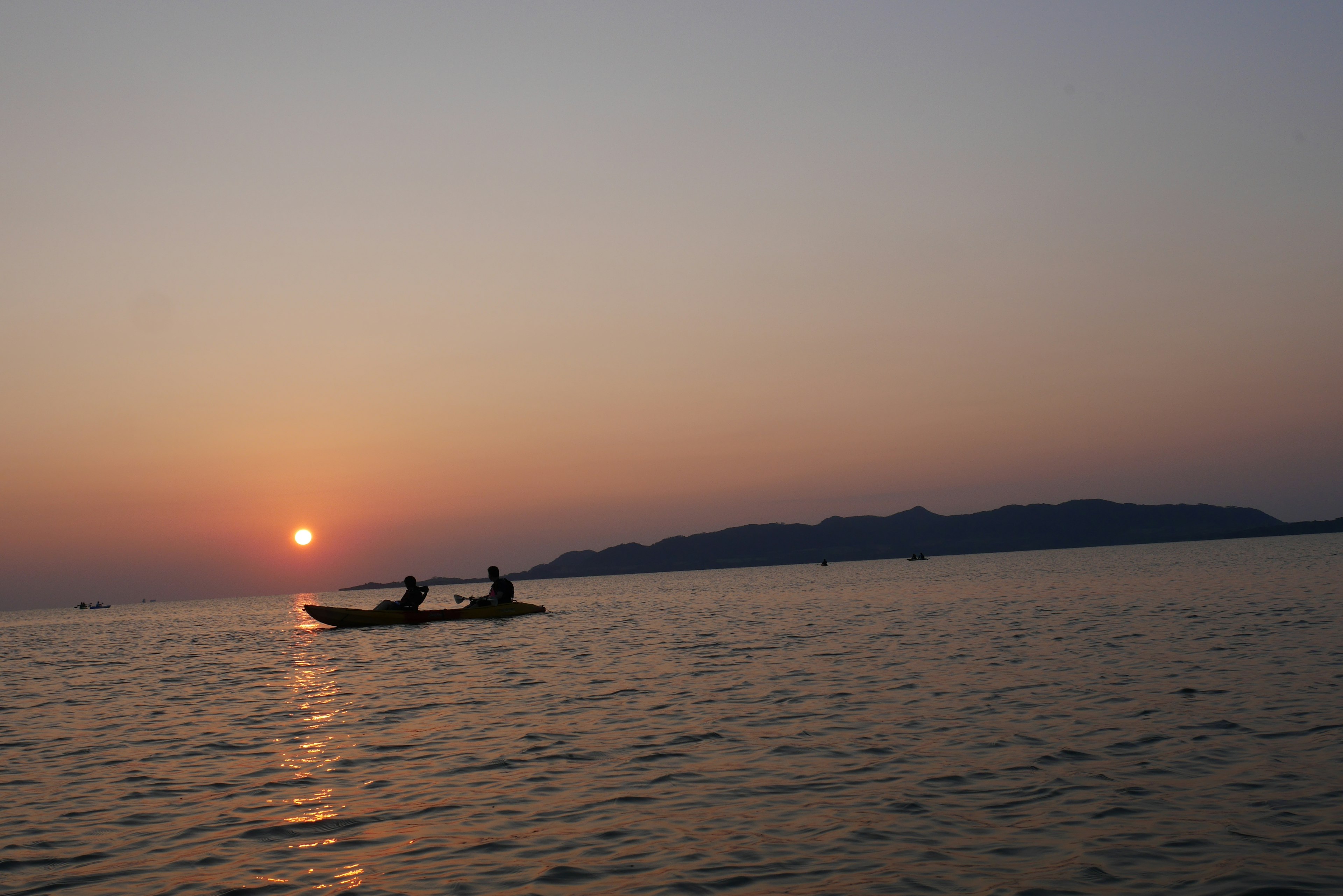 Silhouette of two people in a boat against a sunset on the water