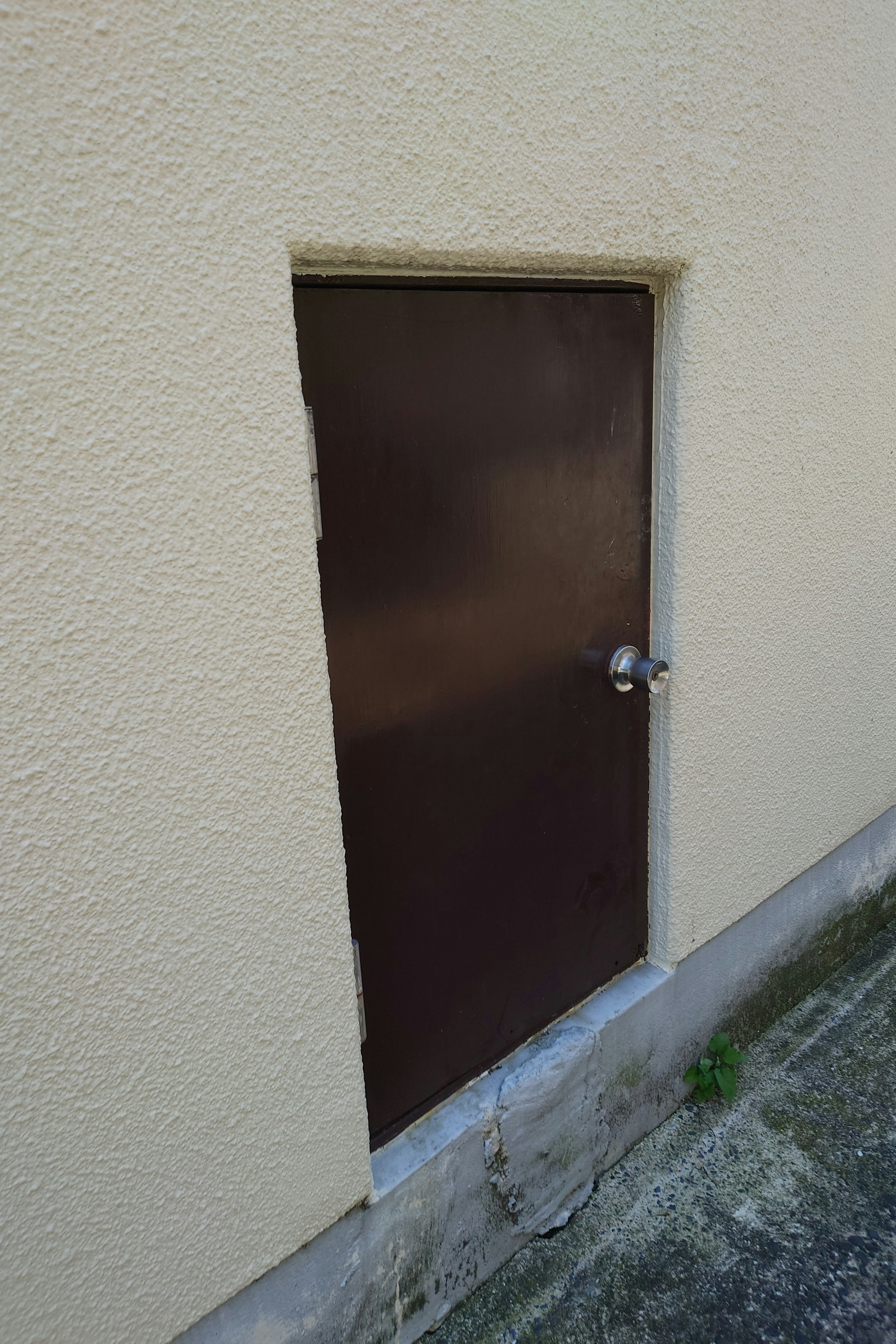 Piccola porta marrone inserita in un muro beige