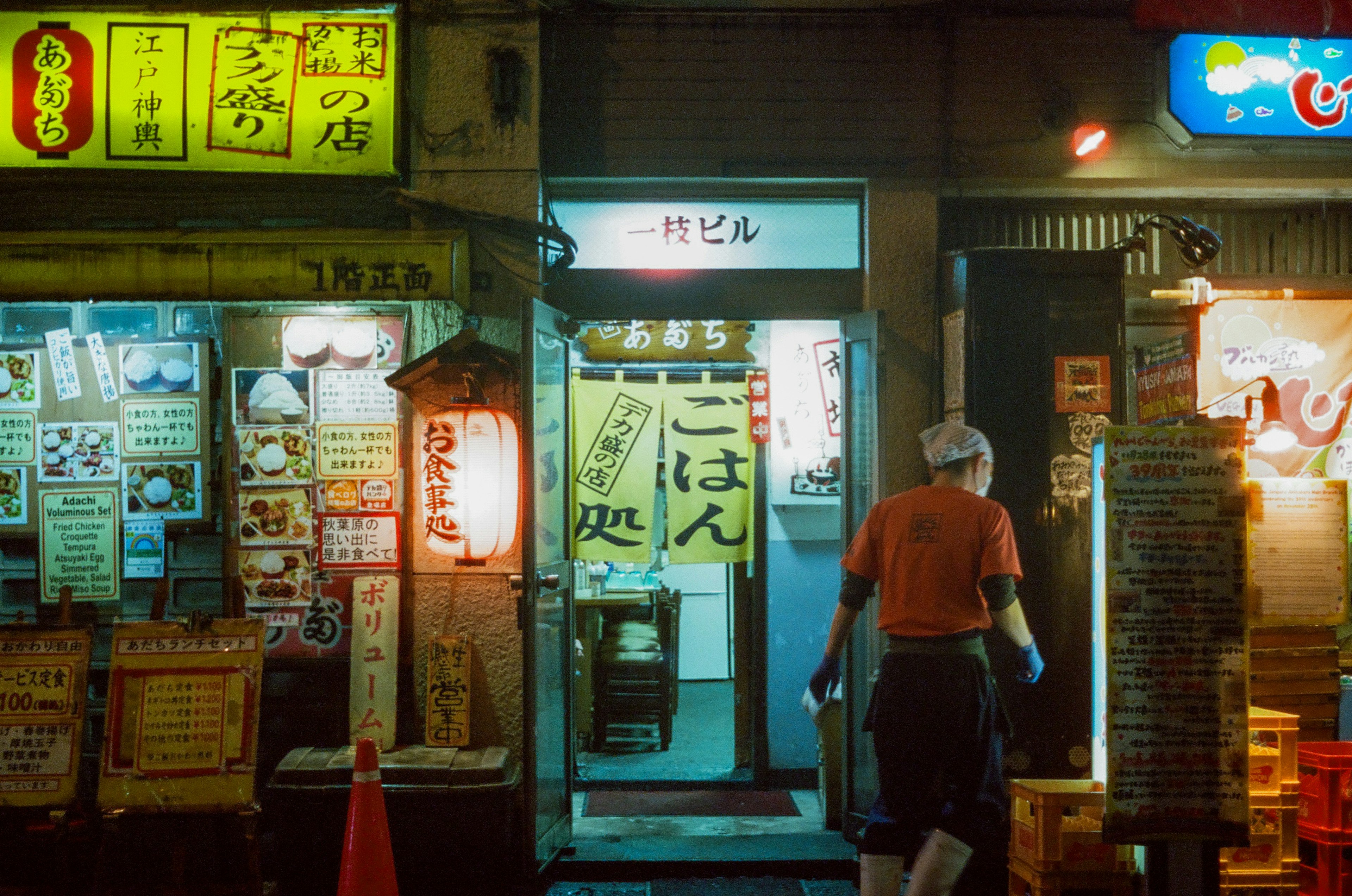 Un hombre entrando a un restaurante en una vibrante calle japonesa por la noche con letreros iluminados