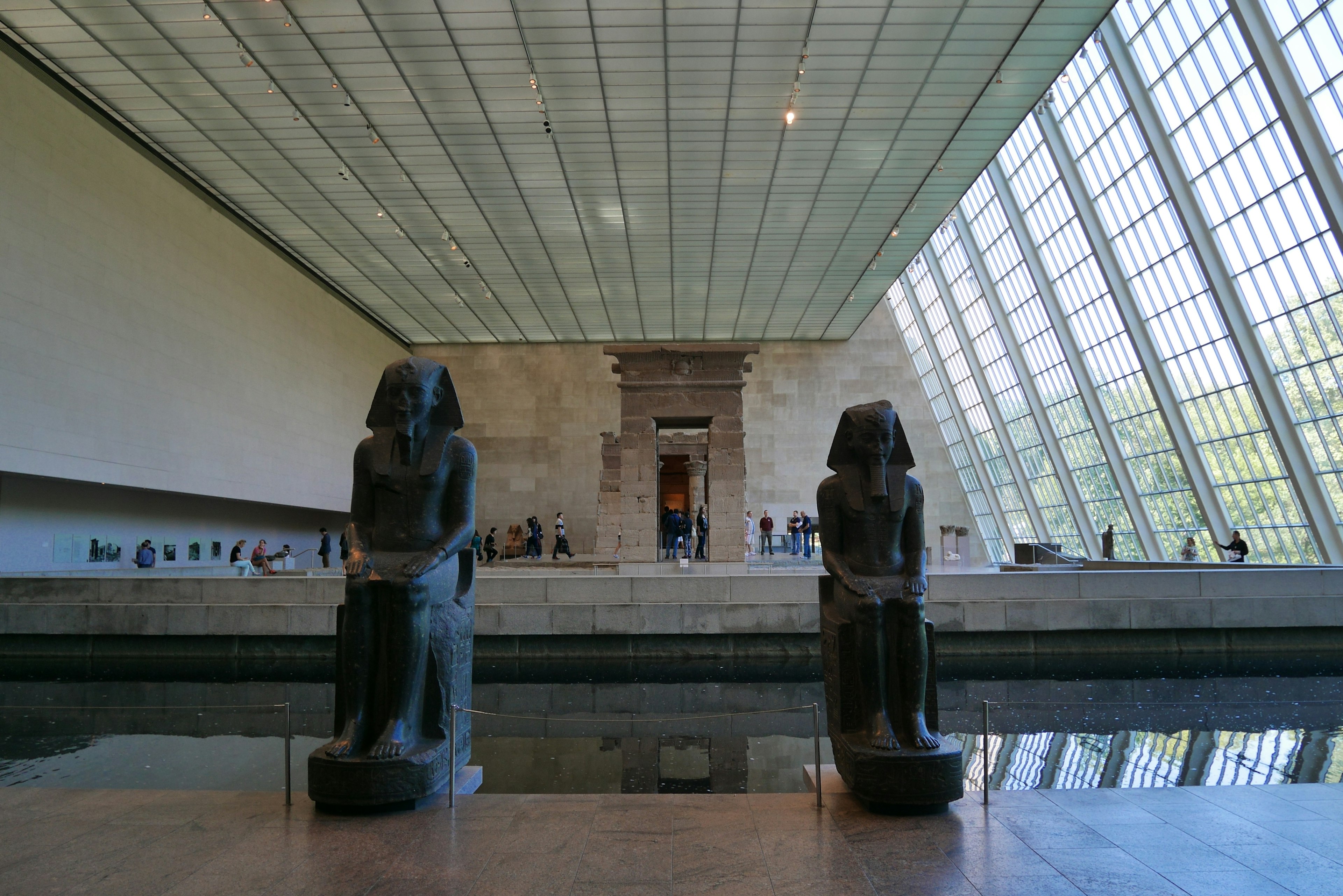 Interior of a museum featuring sphinx sculptures and a glass ceiling with reflections in water