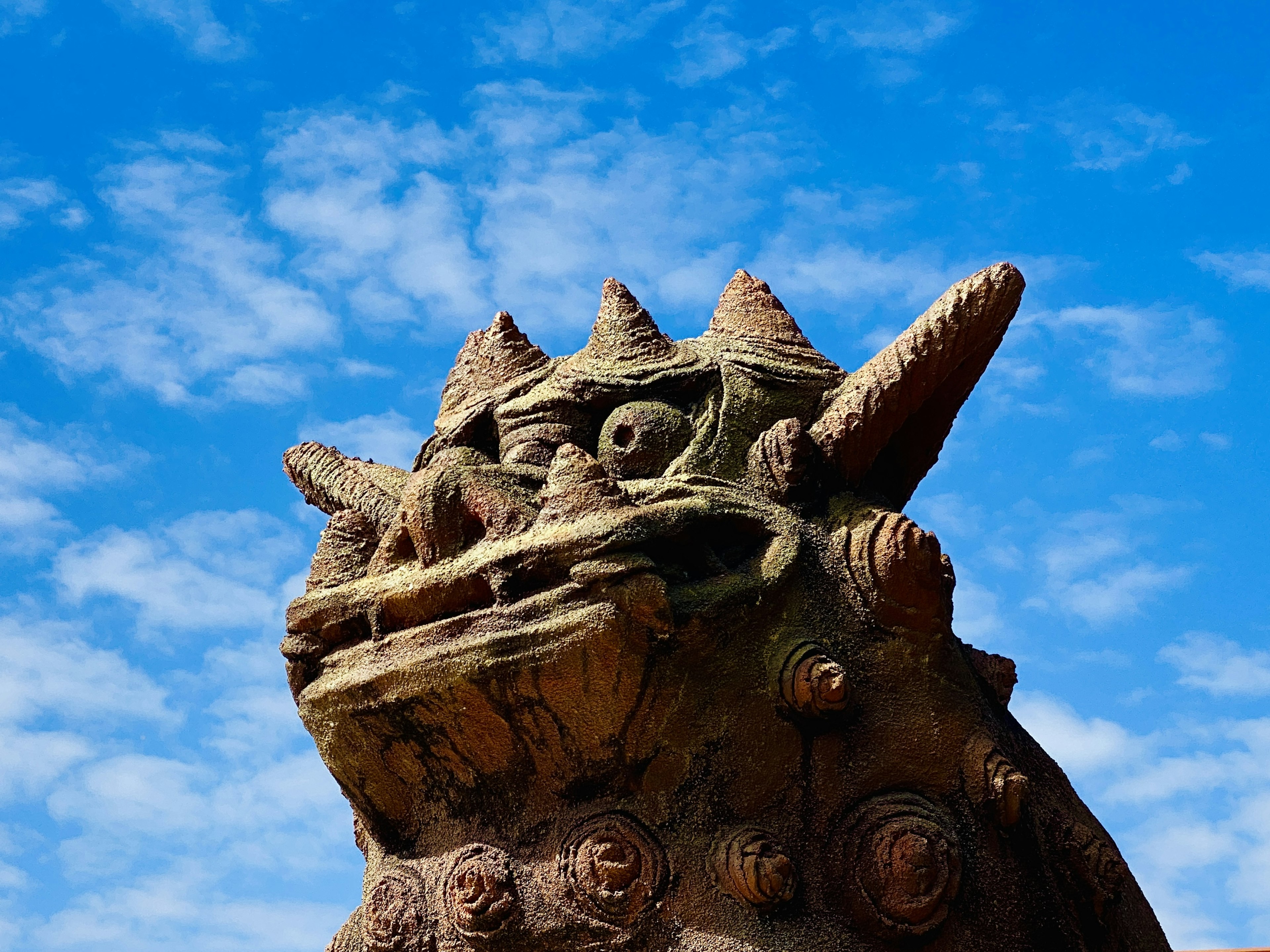 Sculpted dinosaur-like statue head with spiky back against a blue sky