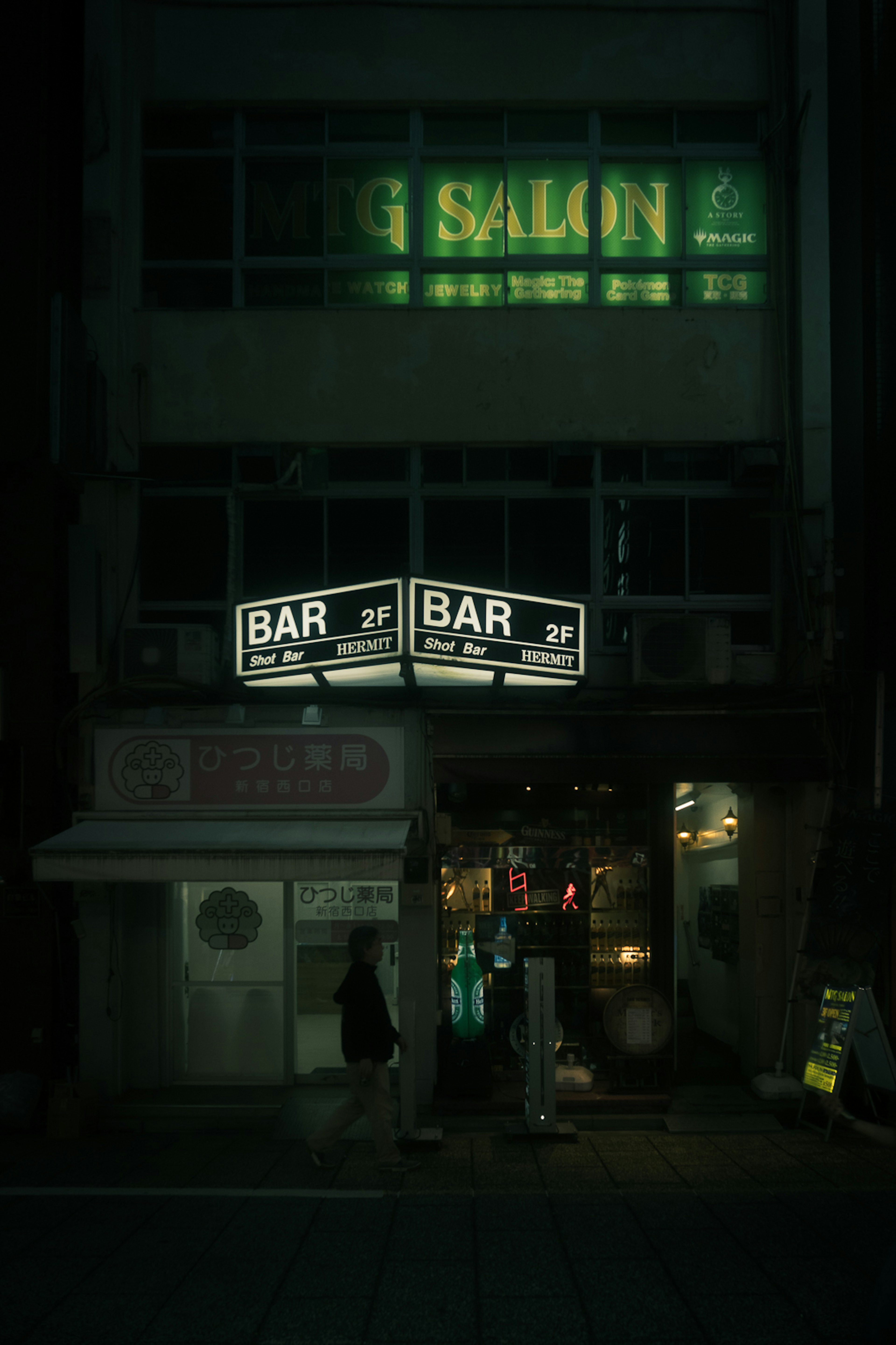 Entrada de un bar con letreros de neón y un salón arriba por la noche