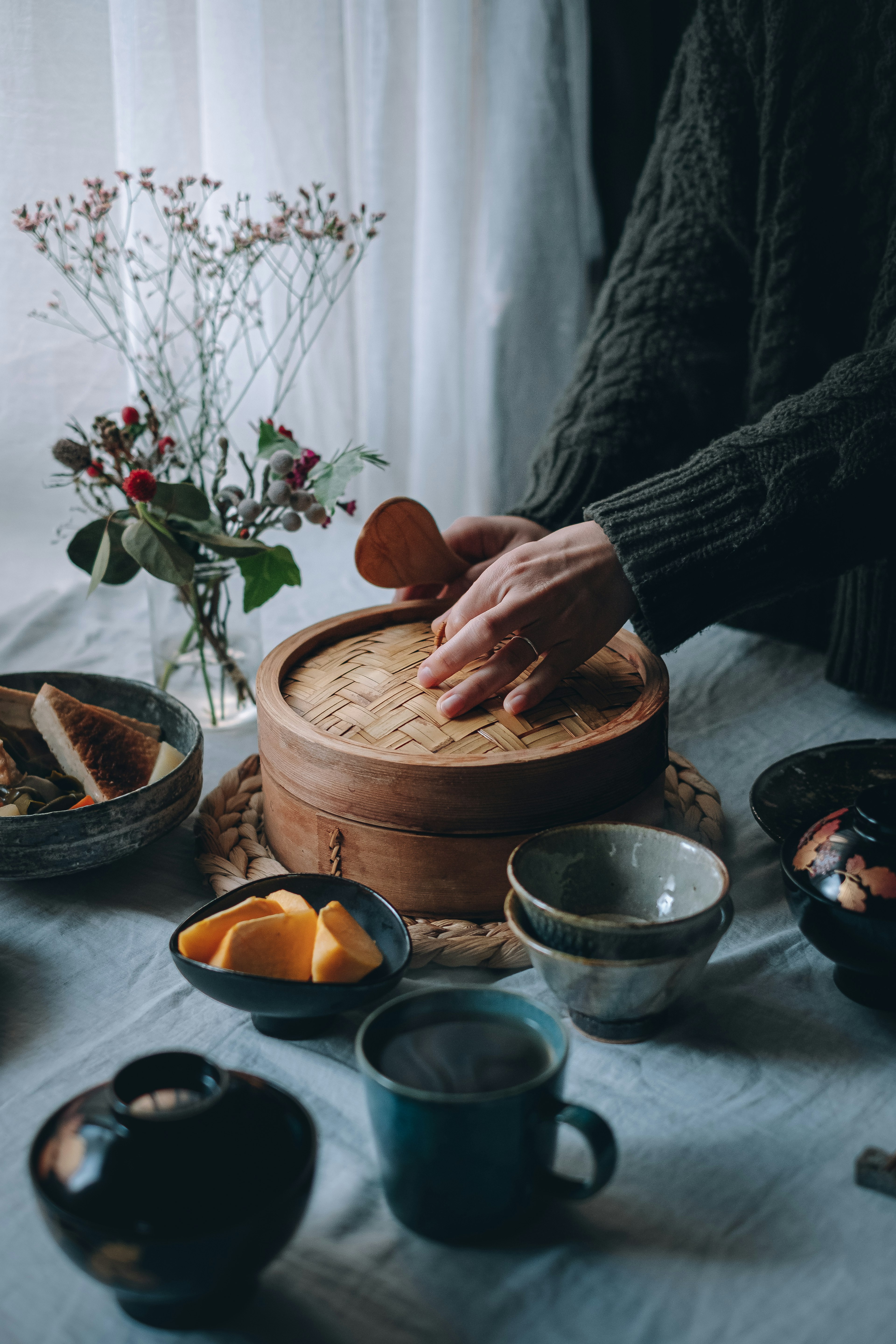 Mains ouvrant un cuiseur en bois sur une table entourée de plats et de fleurs