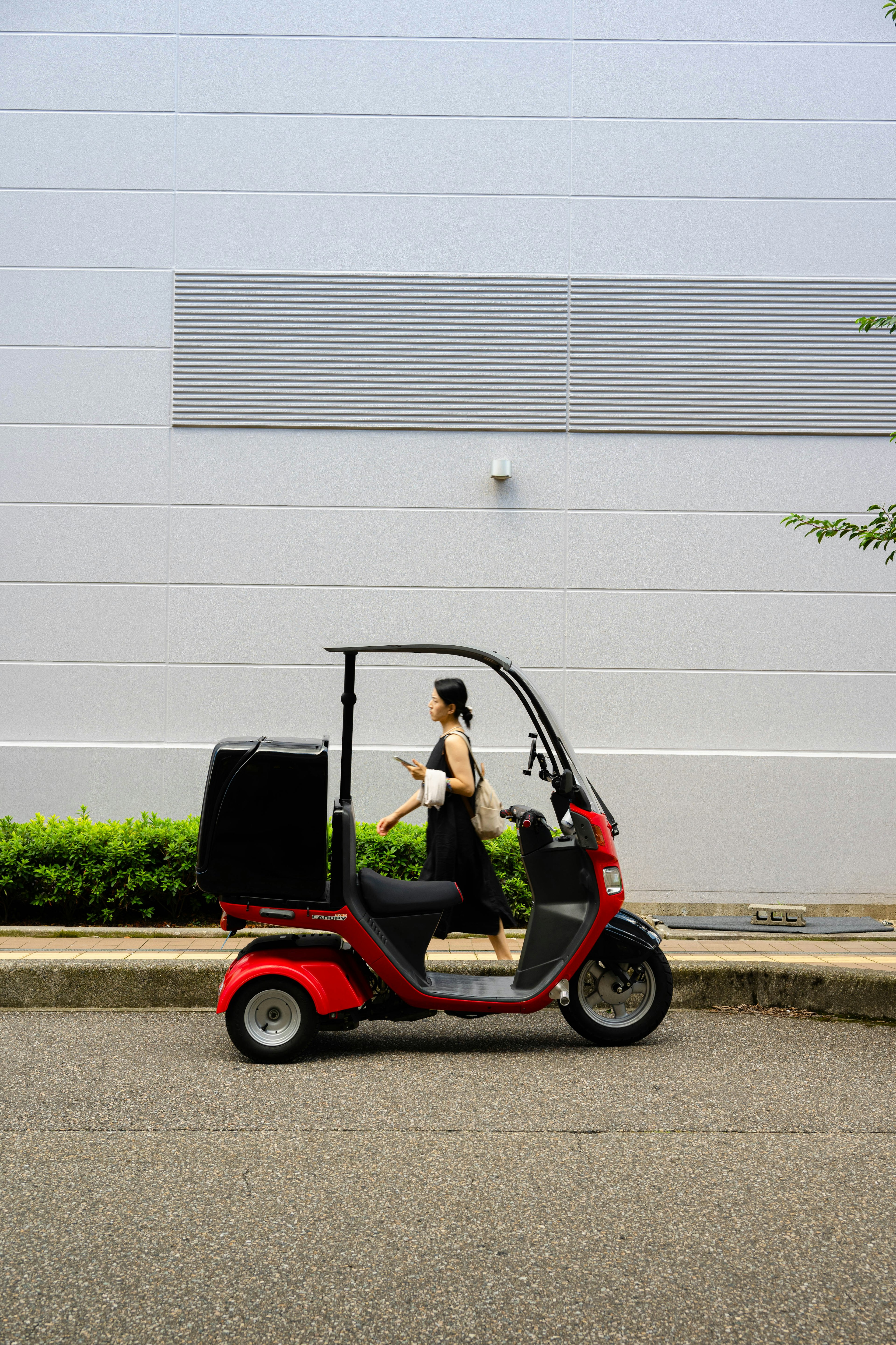 Femme marchant à côté d'un véhicule à trois roues rouge contre un mur gris