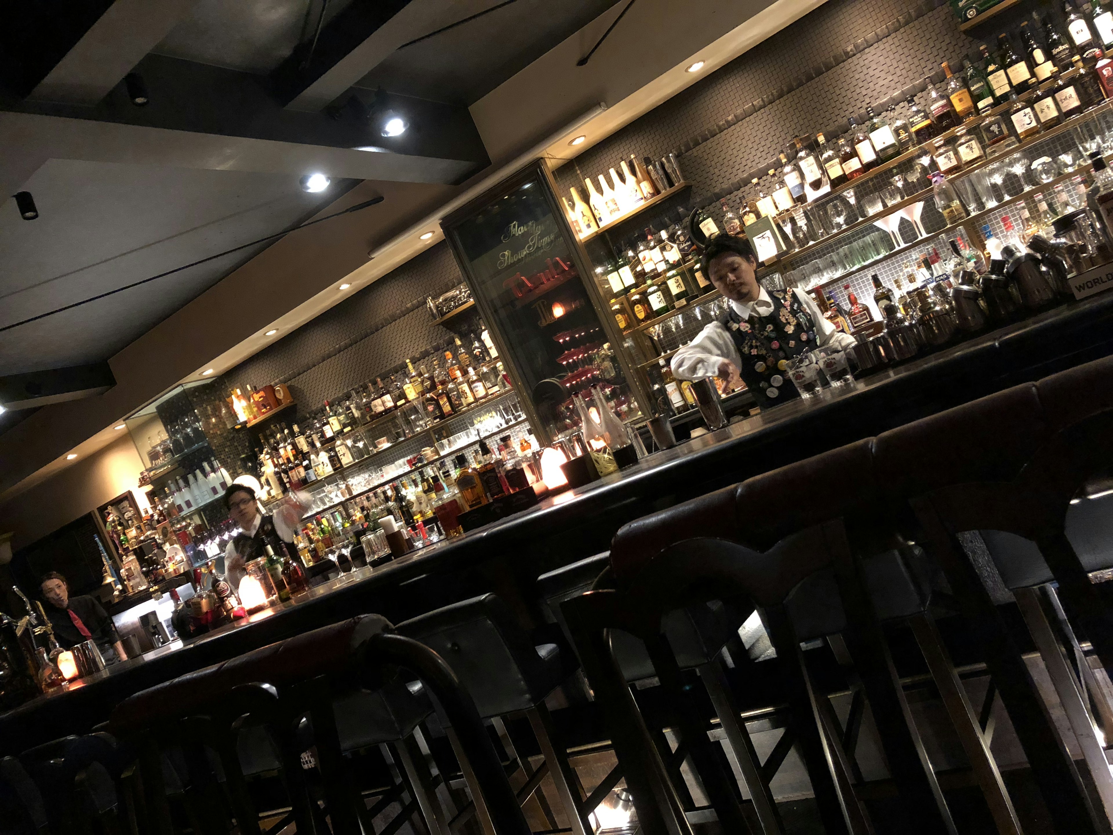 Interior of a bar with a bartender preparing cocktails and shelves filled with bottles