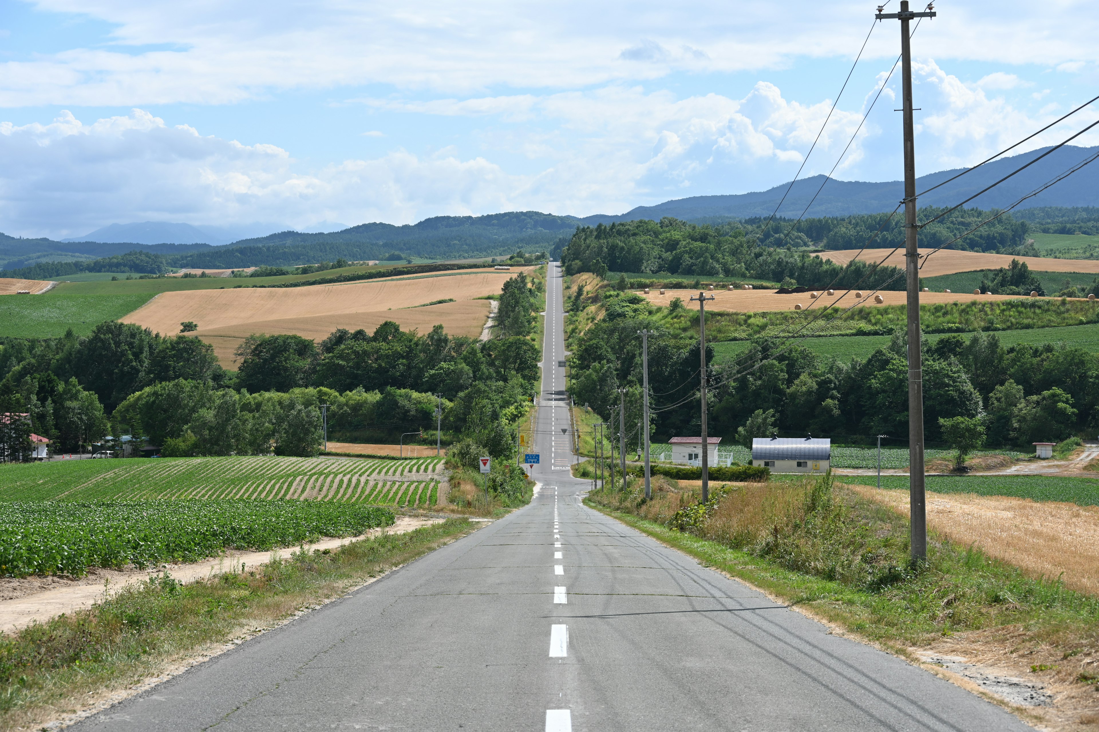 Straight road leading through rural landscape with blue sky