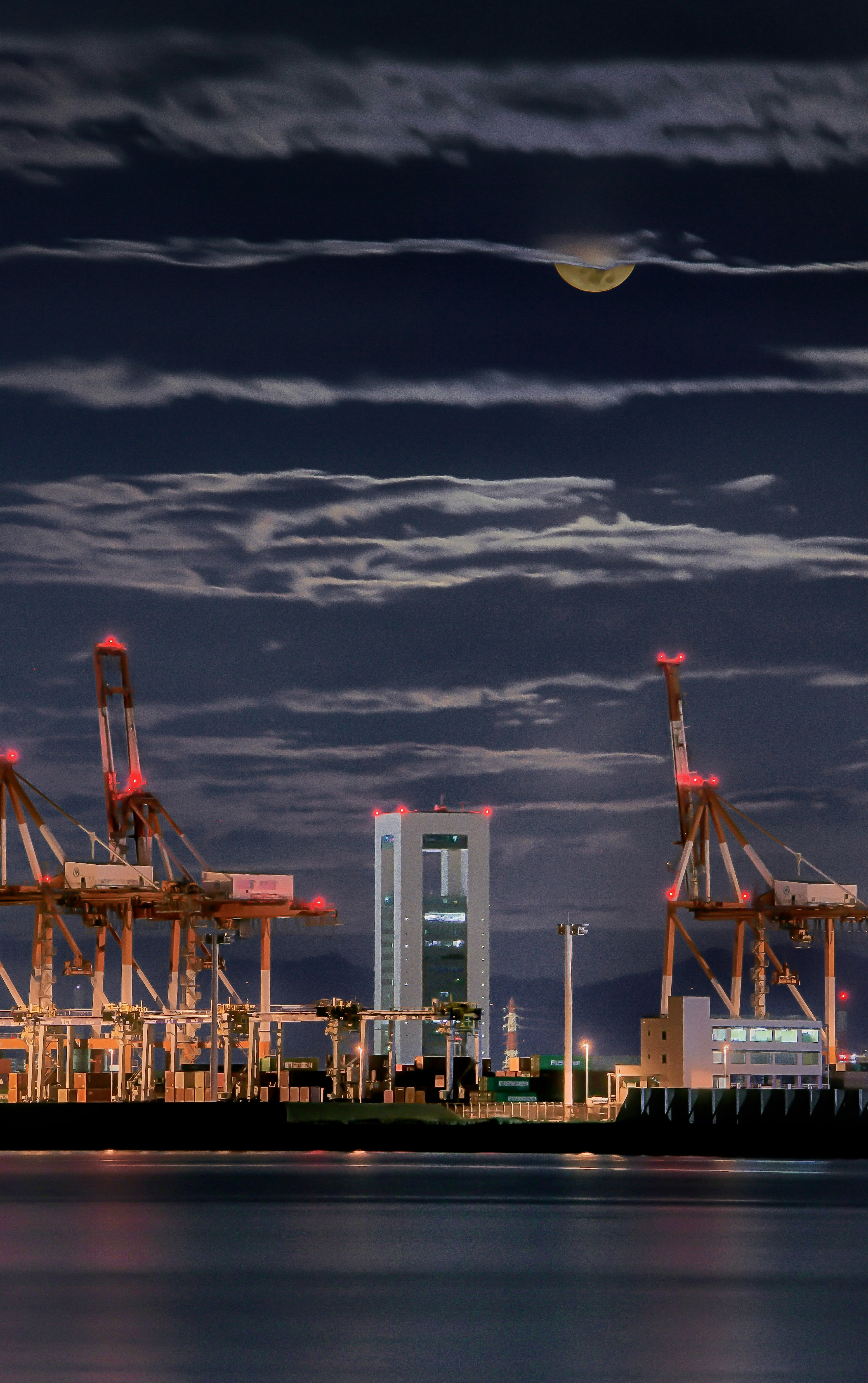 Night sky with a glowing moon above port cranes