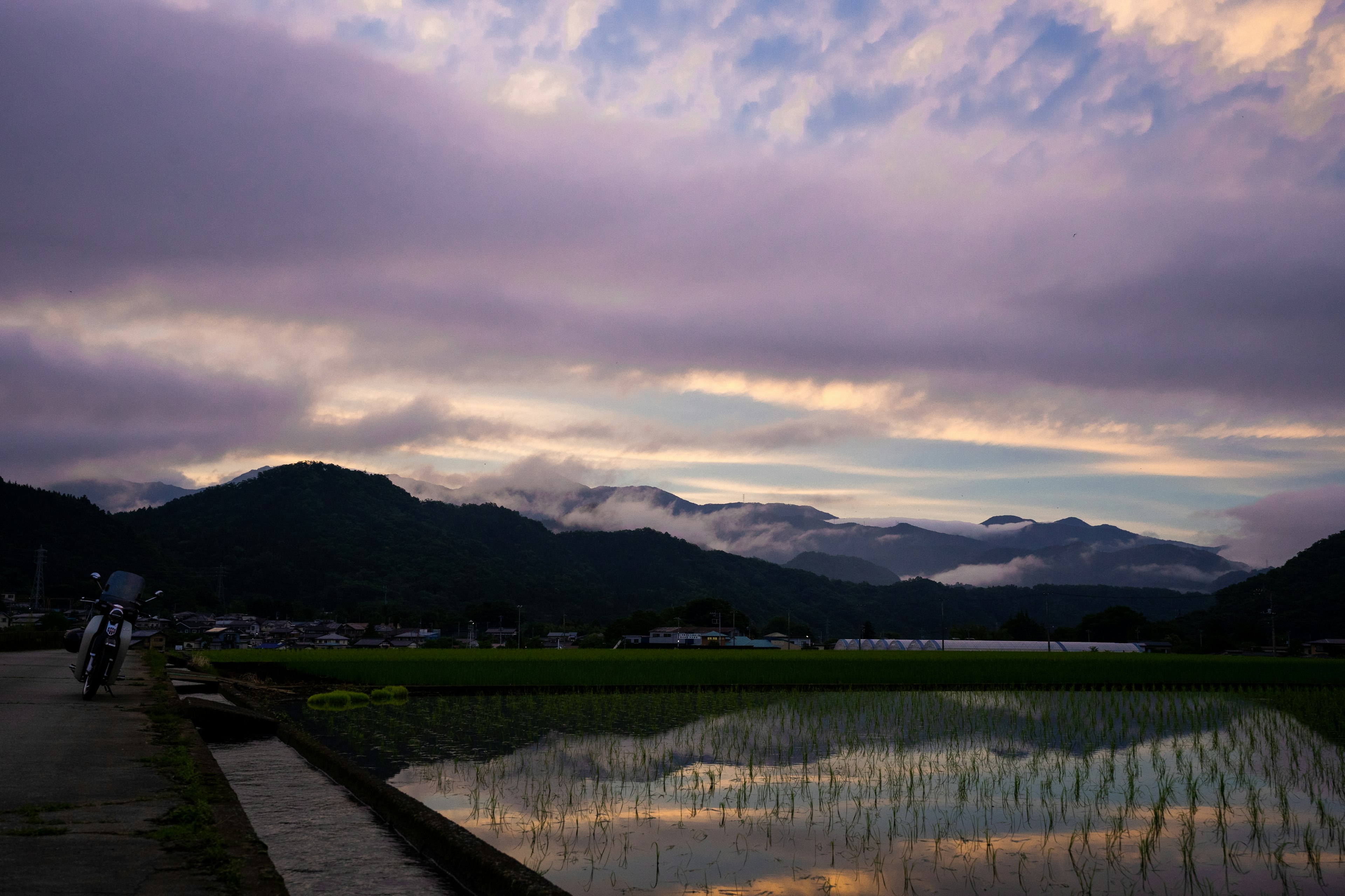 ทิวทัศน์ชนบทที่สวยงามในช่วงพระอาทิตย์ตกพร้อมภูเขาและนาข้าวสะท้อน