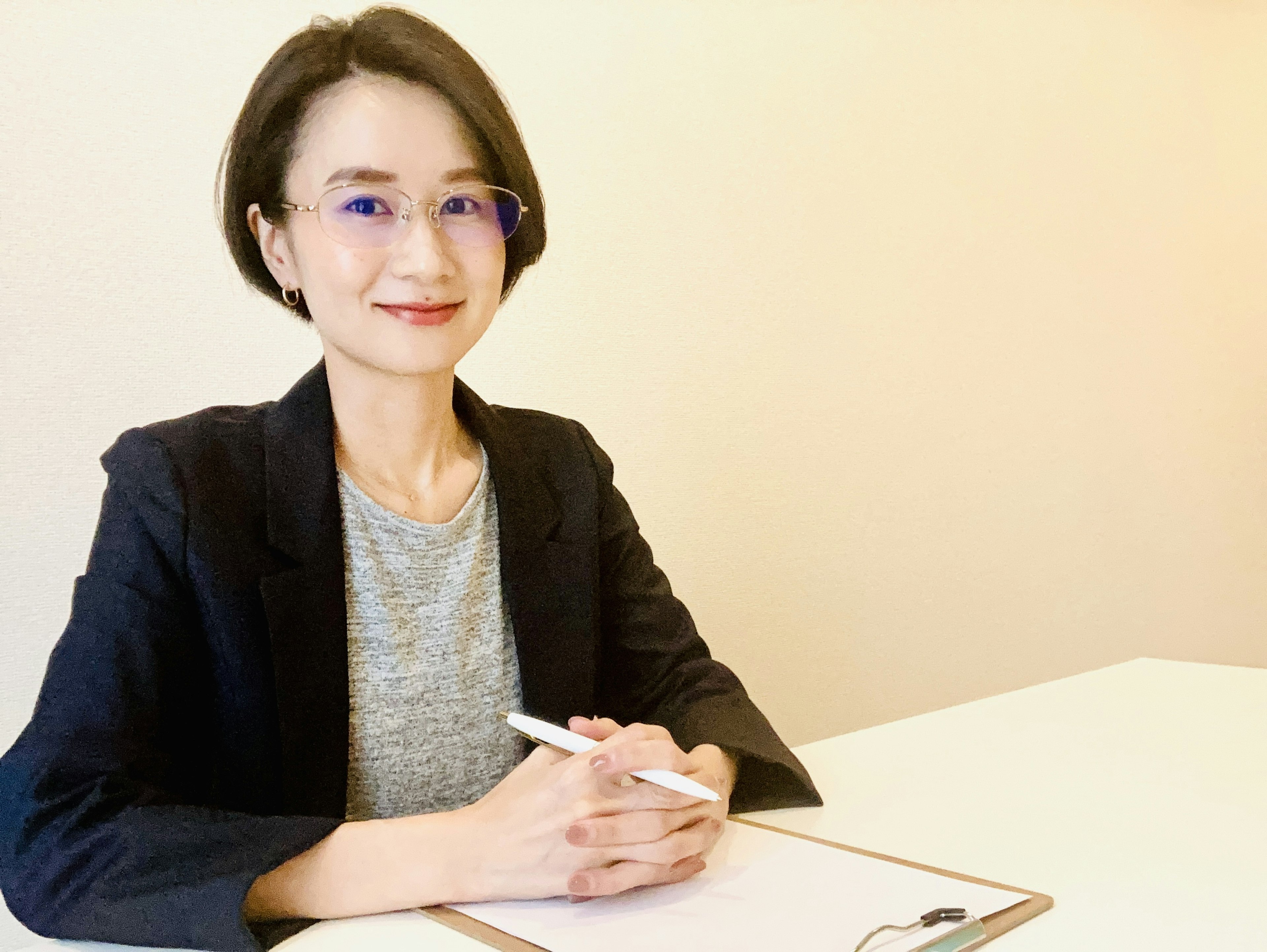 Portrait d'une femme souriante dans un bureau portant un t-shirt gris et un blazer noir avec des lunettes