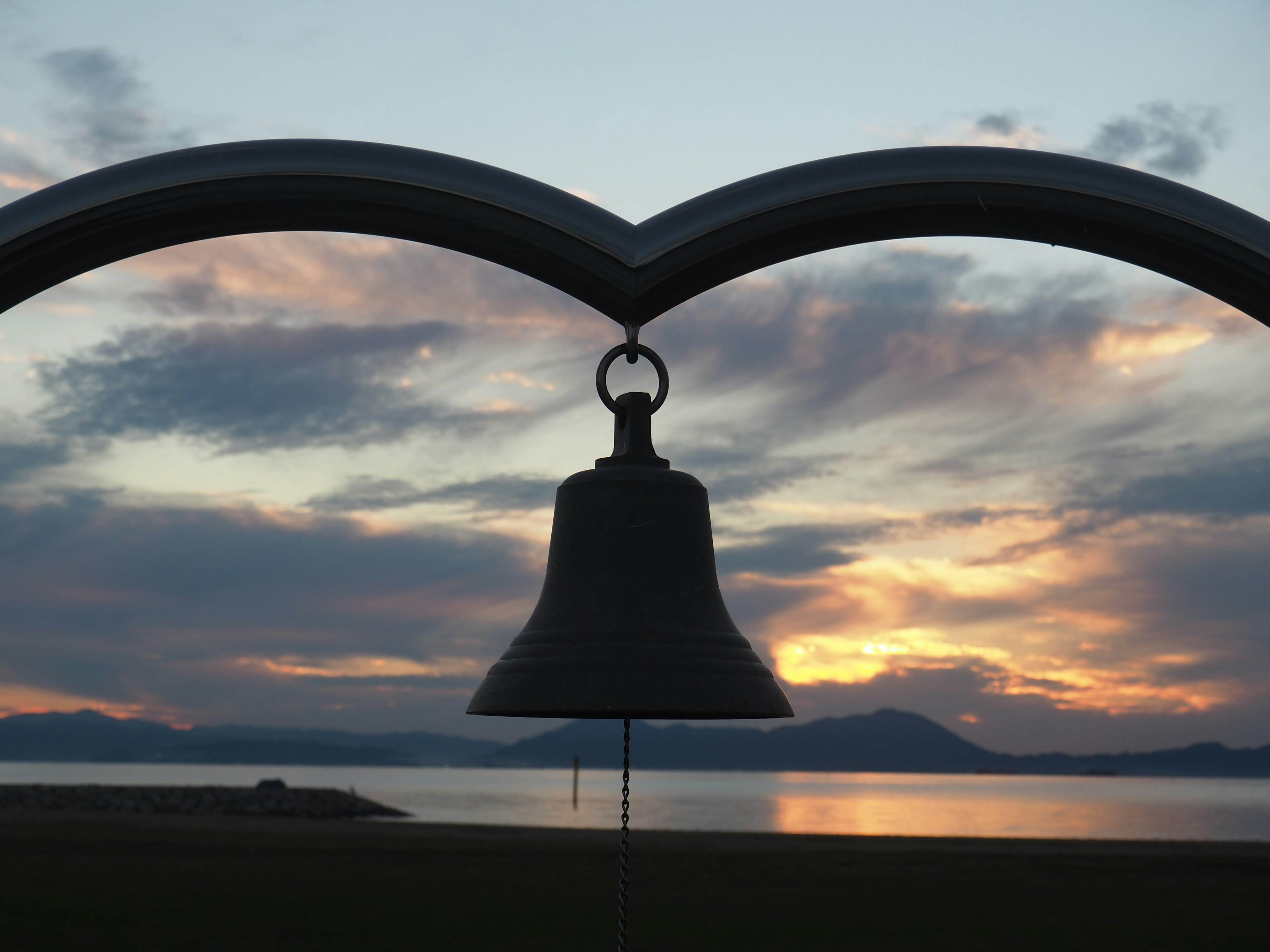 Silhouette einer Glocke vor einem bunten Sonnenuntergangshimmel