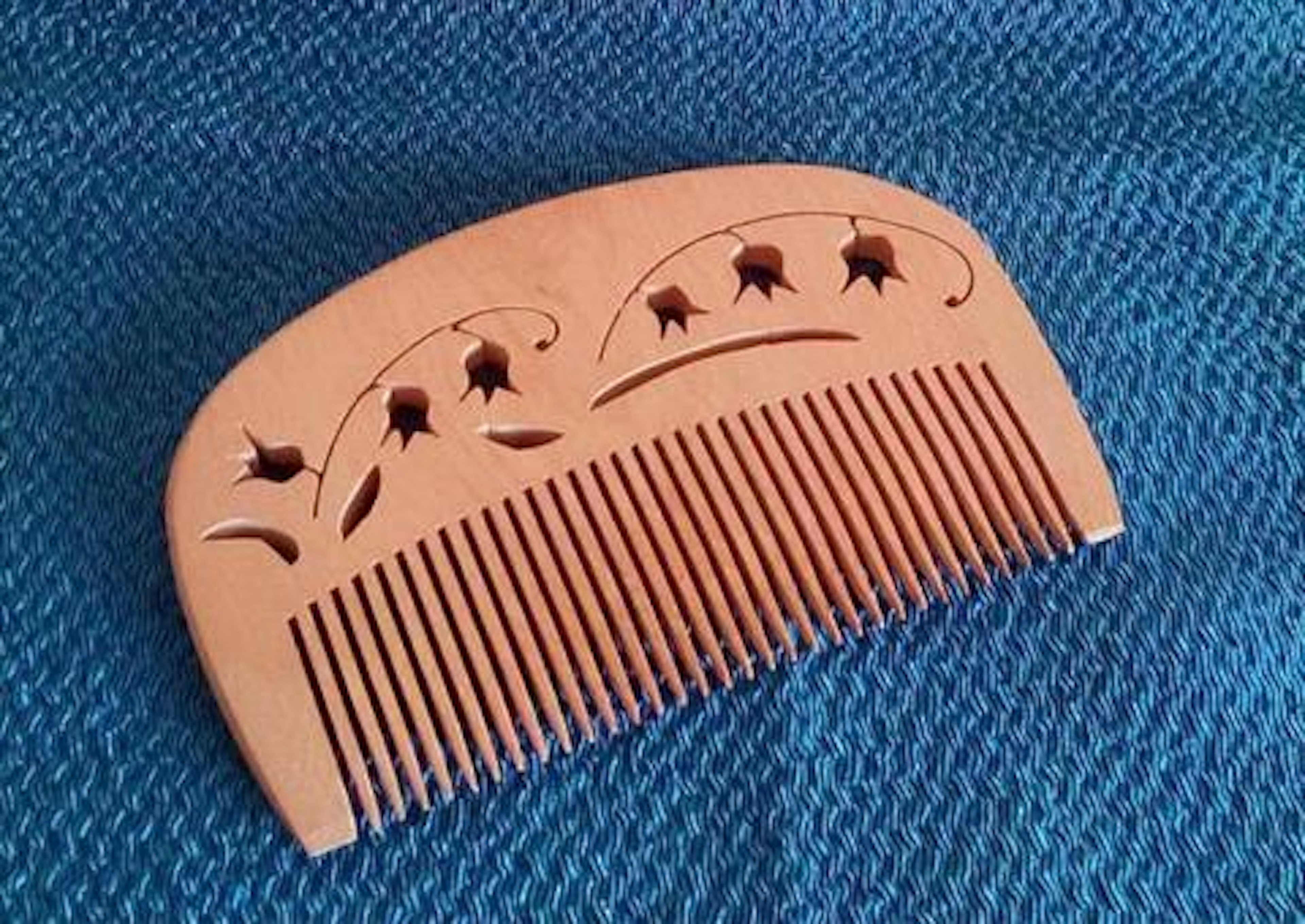 Decorative wooden comb with floral patterns placed on a blue fabric