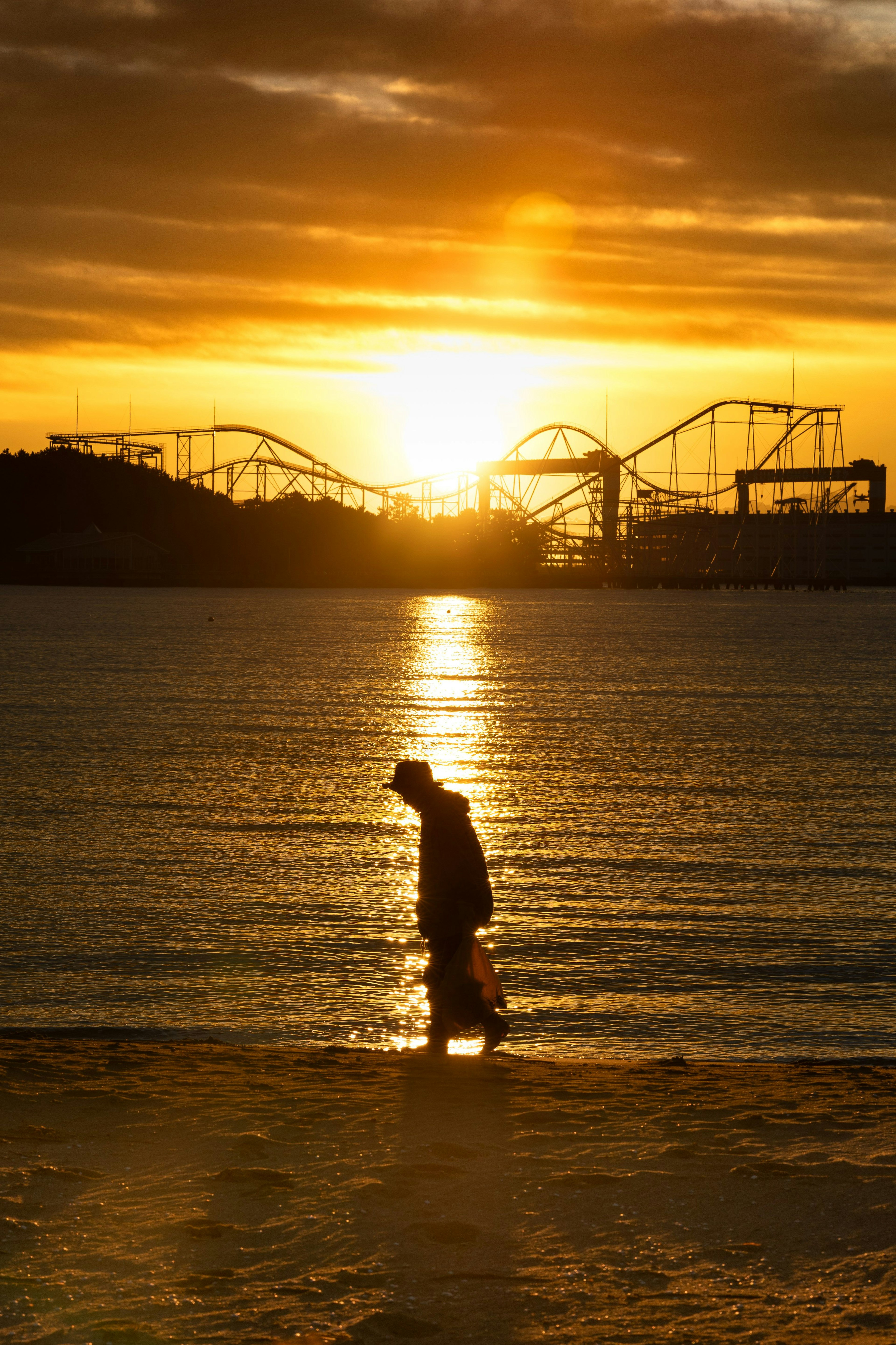 Silhouette d'une personne marchant sur la plage au coucher du soleil avec un parc d'attractions en arrière-plan