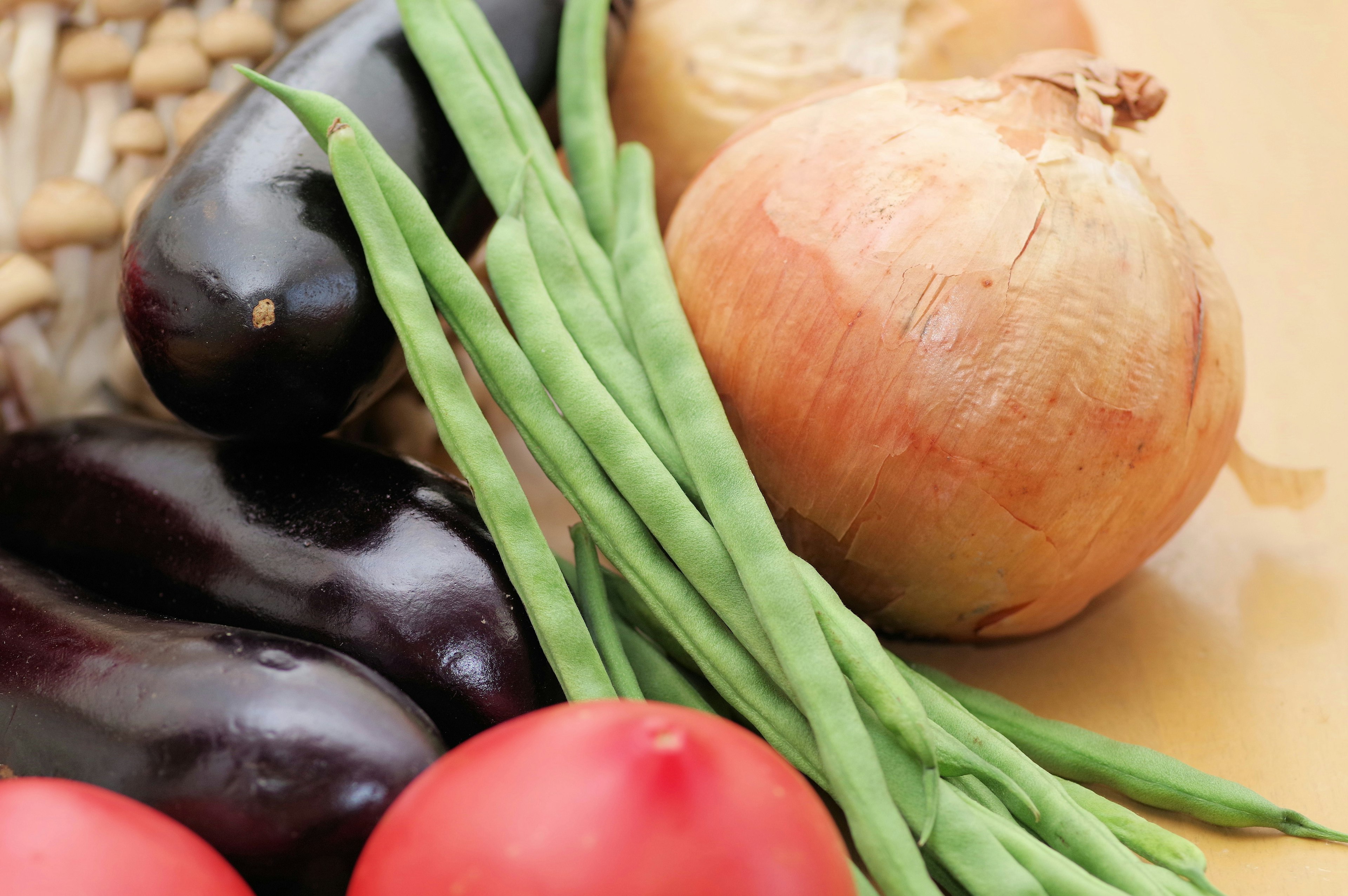 Verdure colorate disposte su un tavolo con melanzane pomodori fagiolini e una cipolla