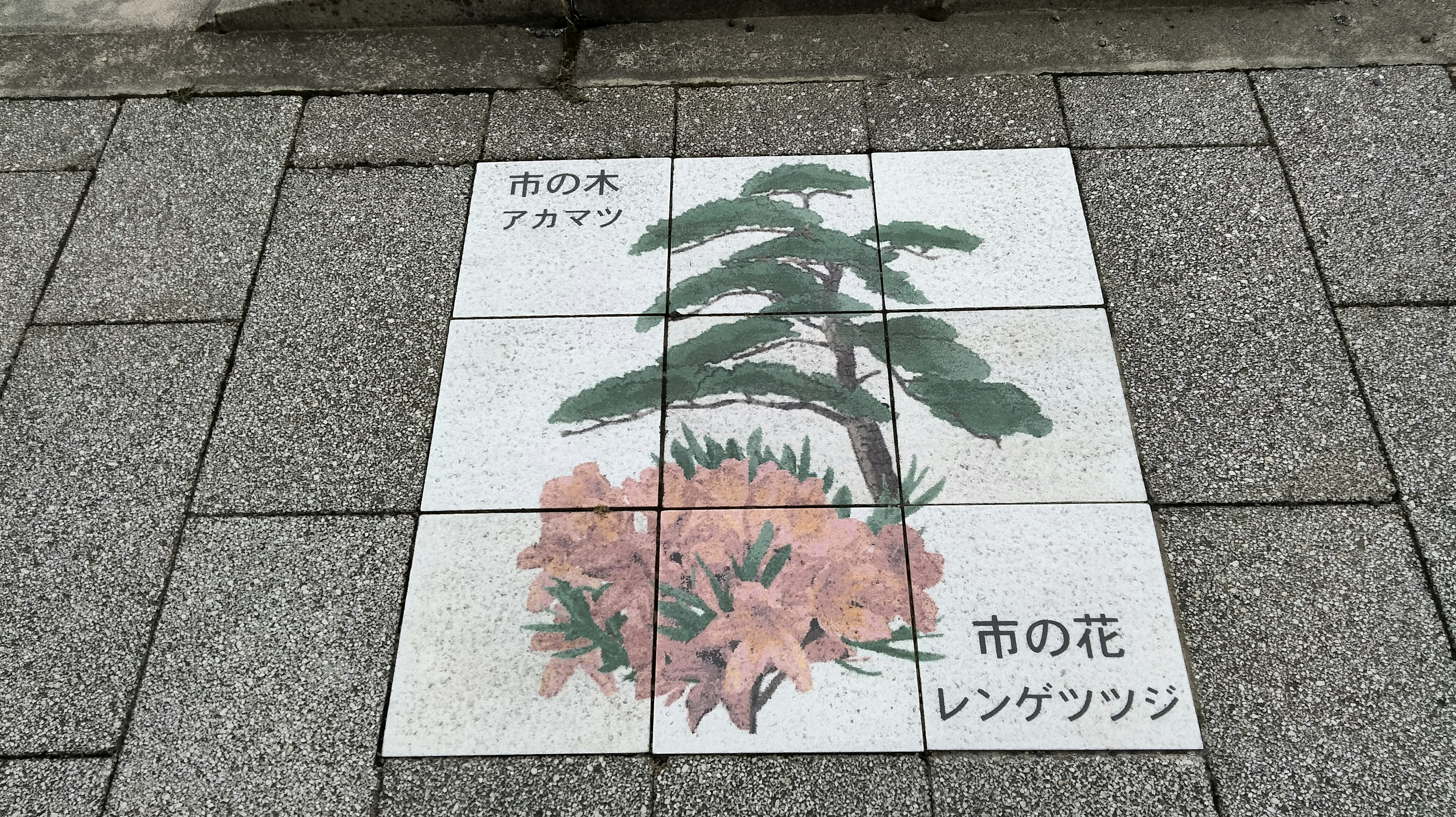 Arte en azulejos en el pavimento con flores rosas y un pino