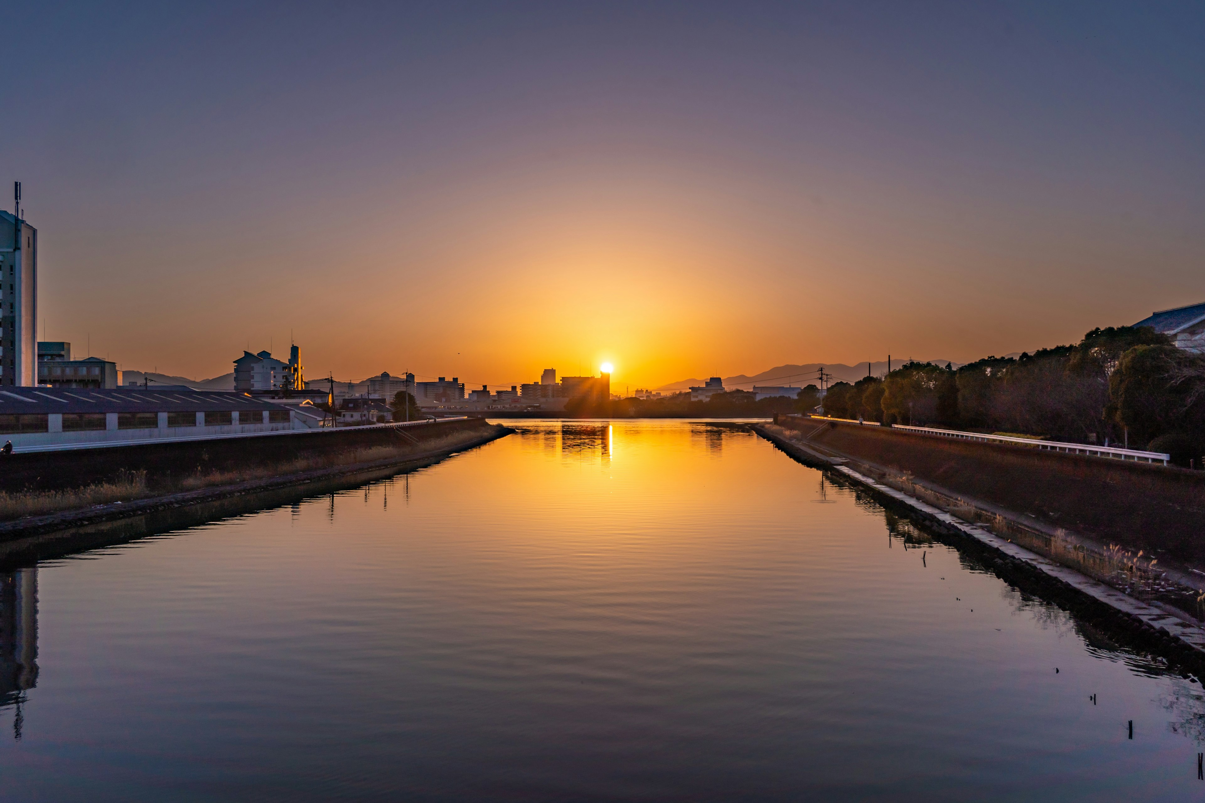 Paesaggio fluviale sereno con il tramonto che si riflette sull'acqua e la silhouette della città