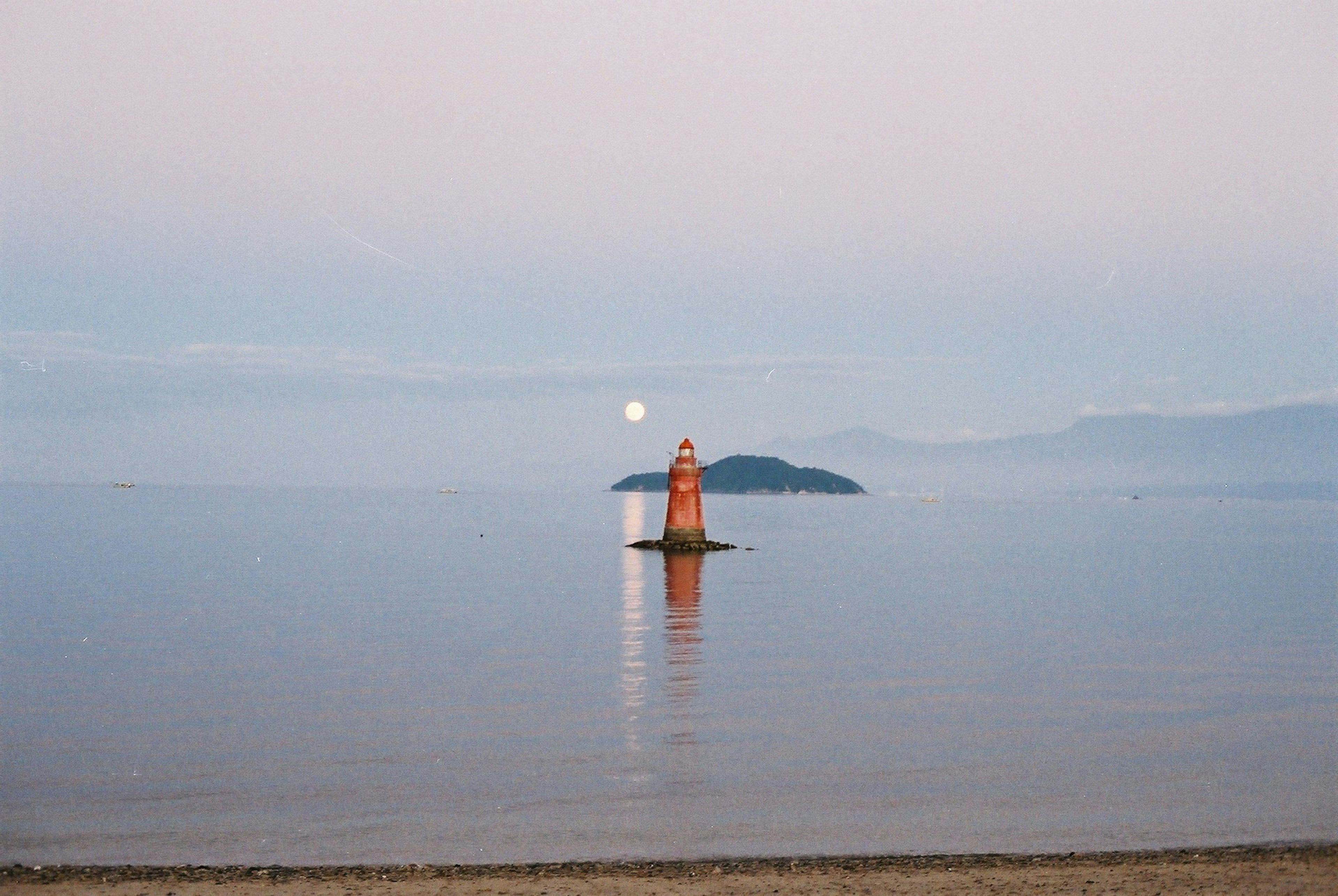 Faro rojo de pie en mar en calma con suave luz de luna