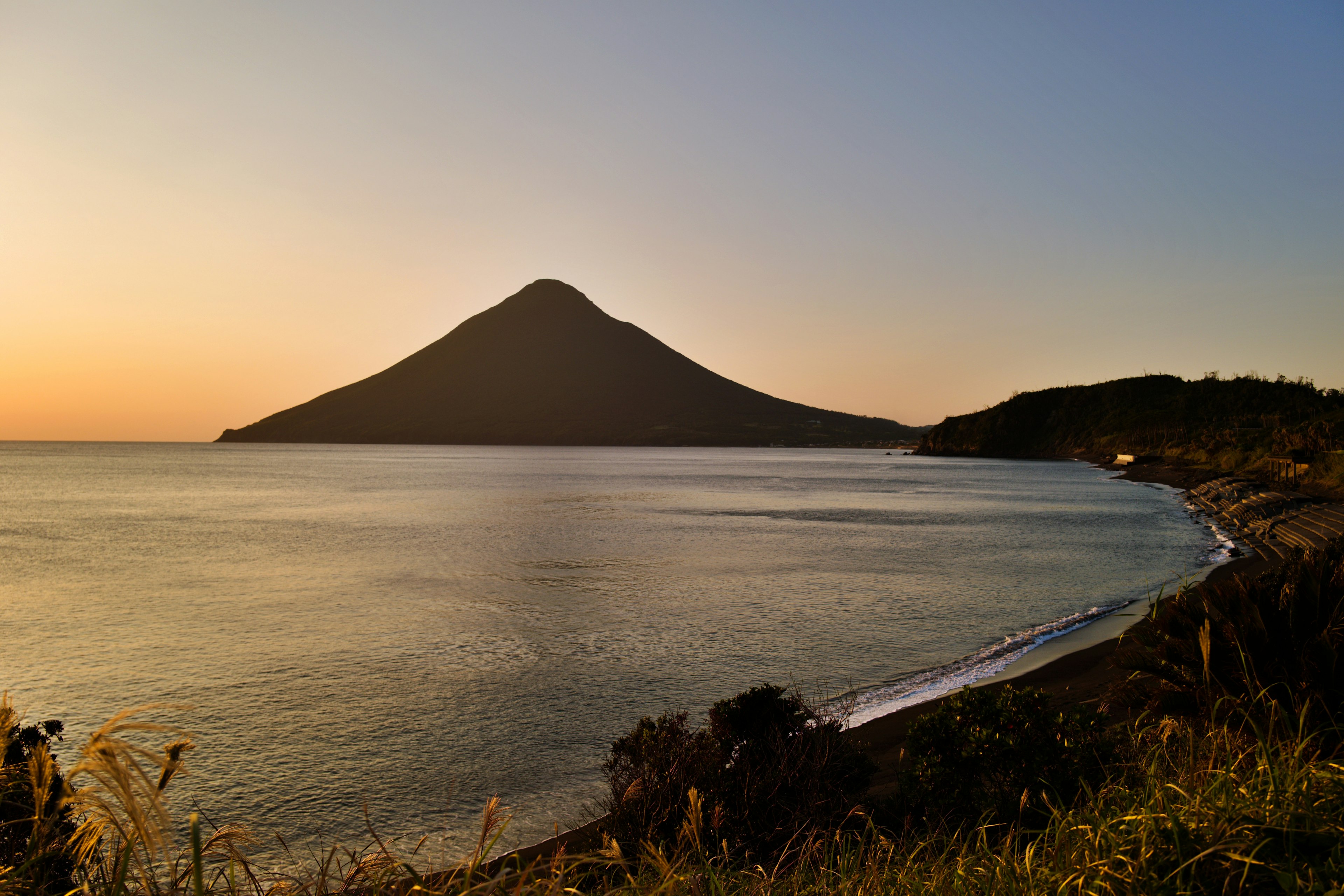 Wunderschöner Berg, der über ruhigem Meer bei Sonnenuntergang aufragt