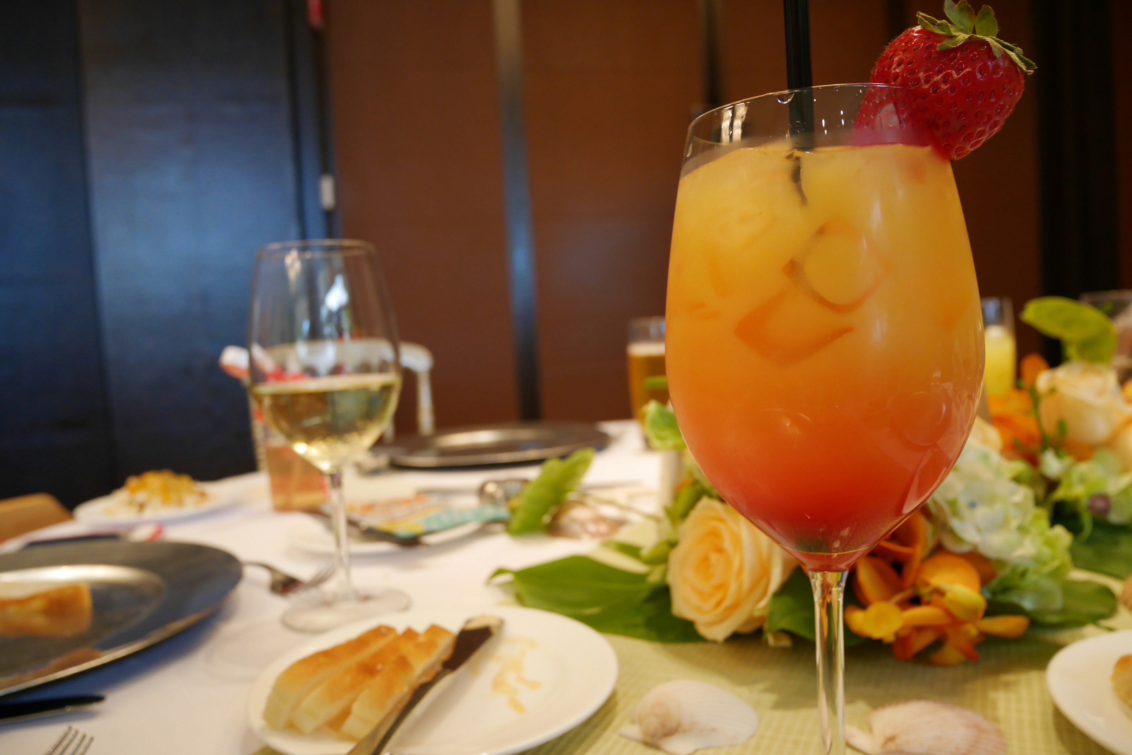 A cocktail glass with a gradient color and a strawberry garnish on a dining table