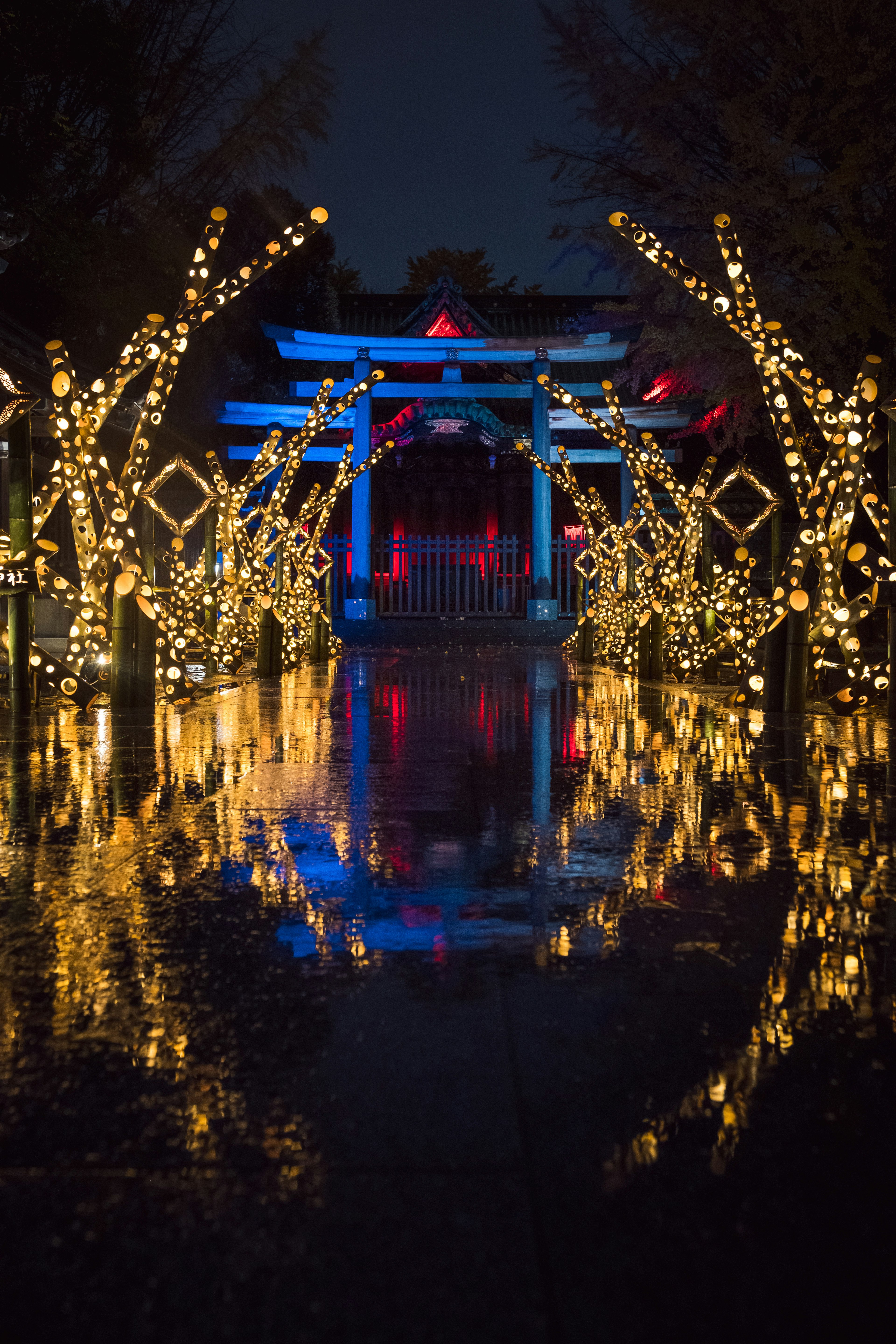 Illuminated shrine gate surrounded by glowing lights with reflections on water at night