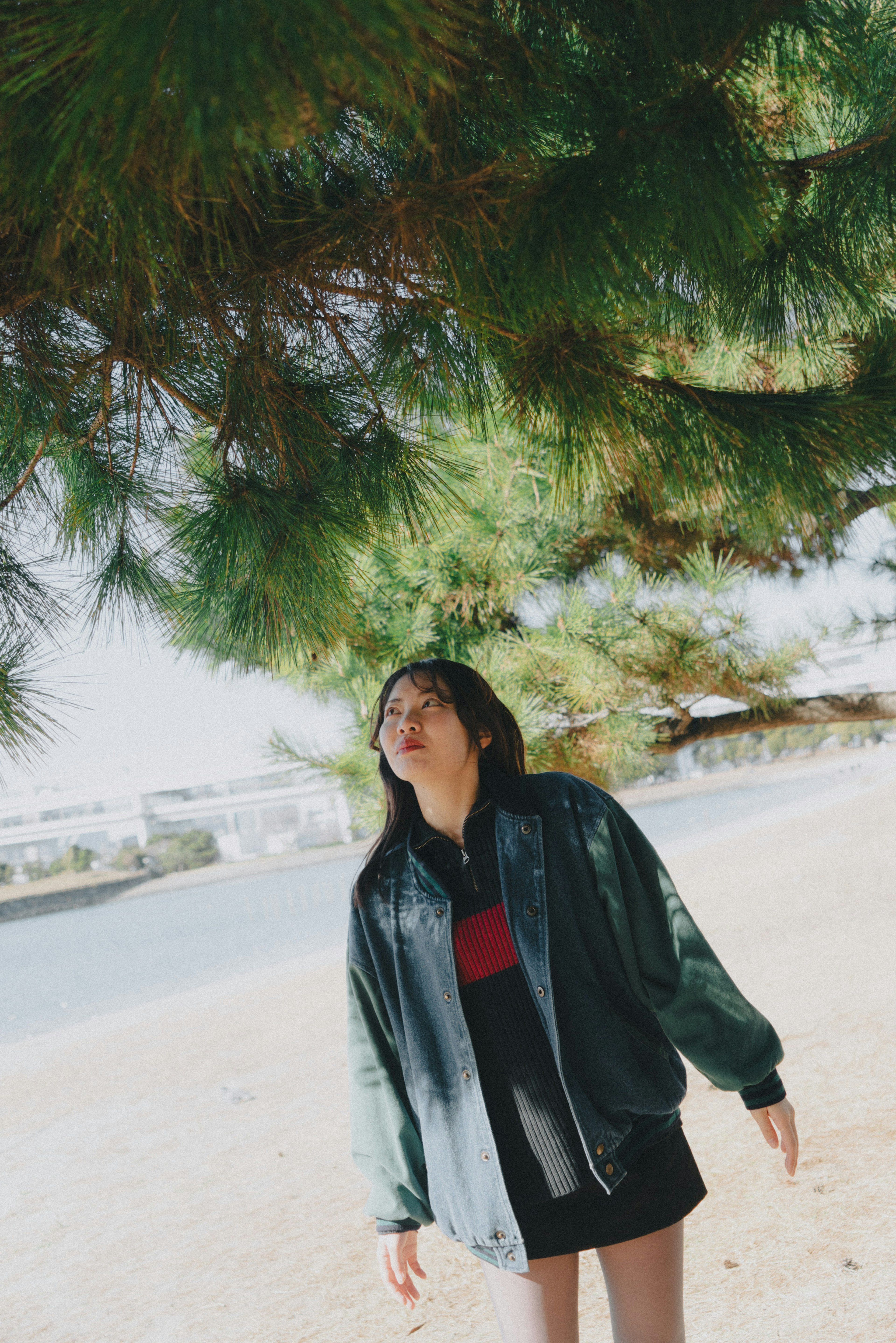 Woman standing under a green tree by the beach