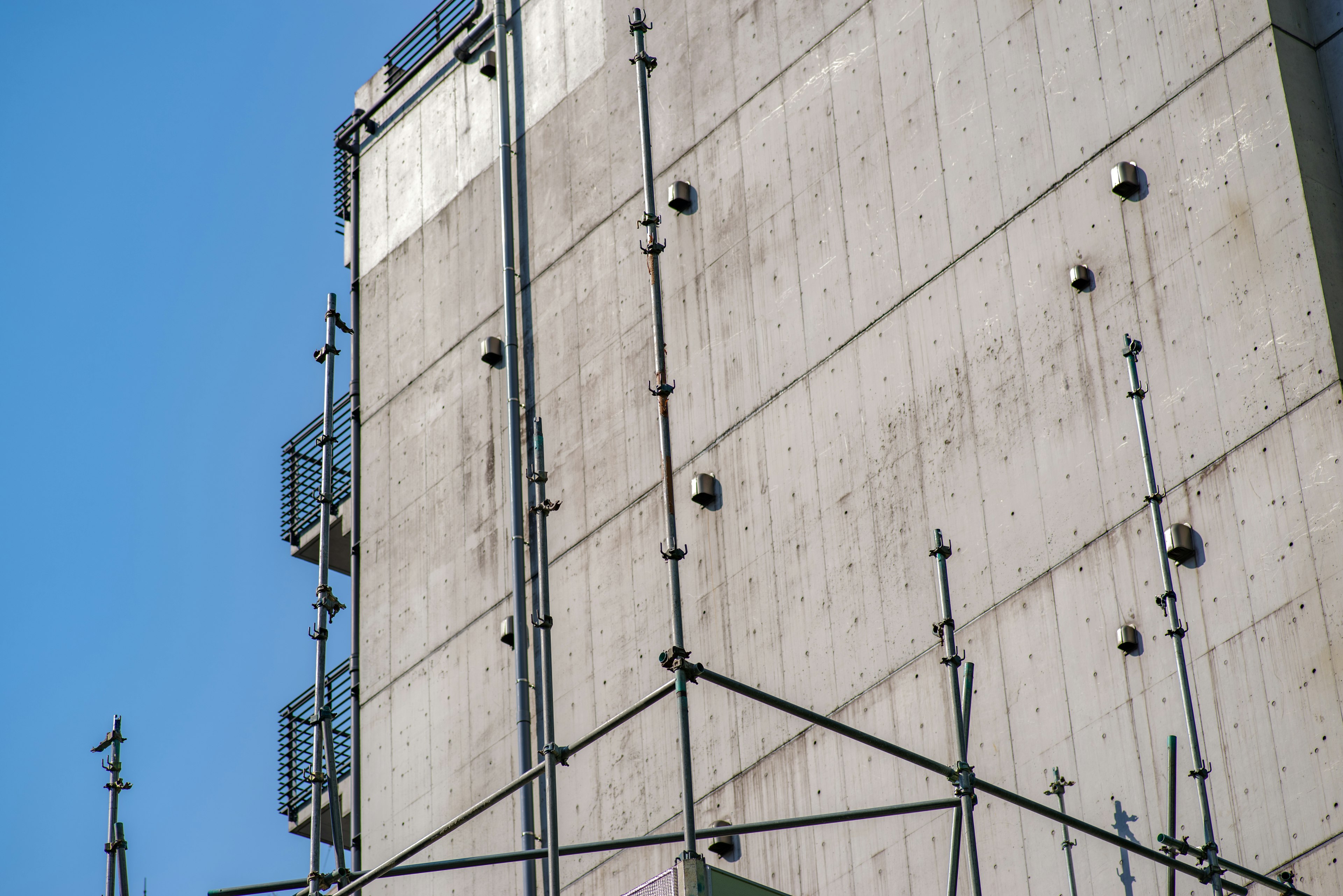 Betonwand eines Gebäudes mit sichtbaren Metallstrukturen und -elementen