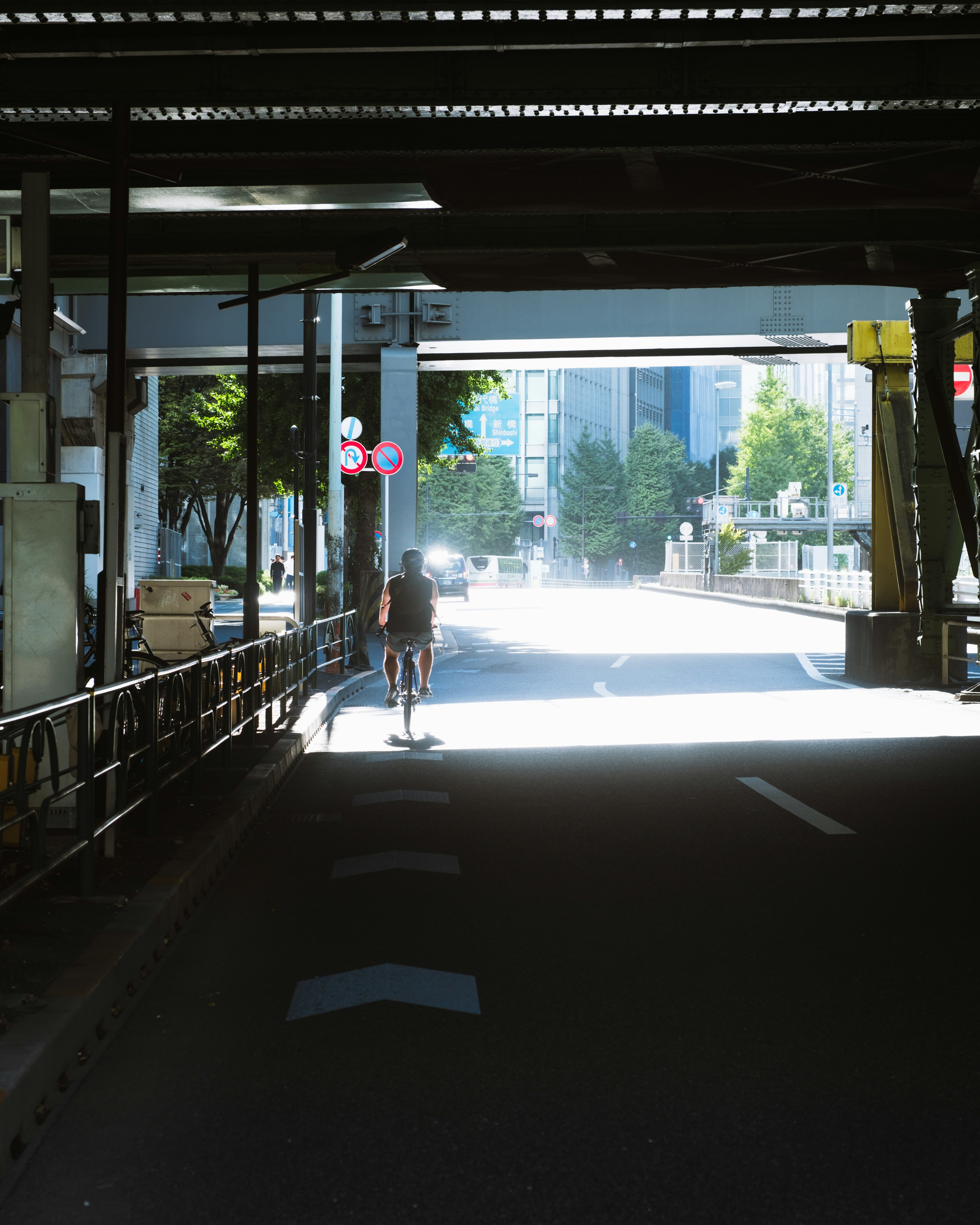 Persona caminando hacia una luz brillante bajo un paso elevado en un entorno urbano