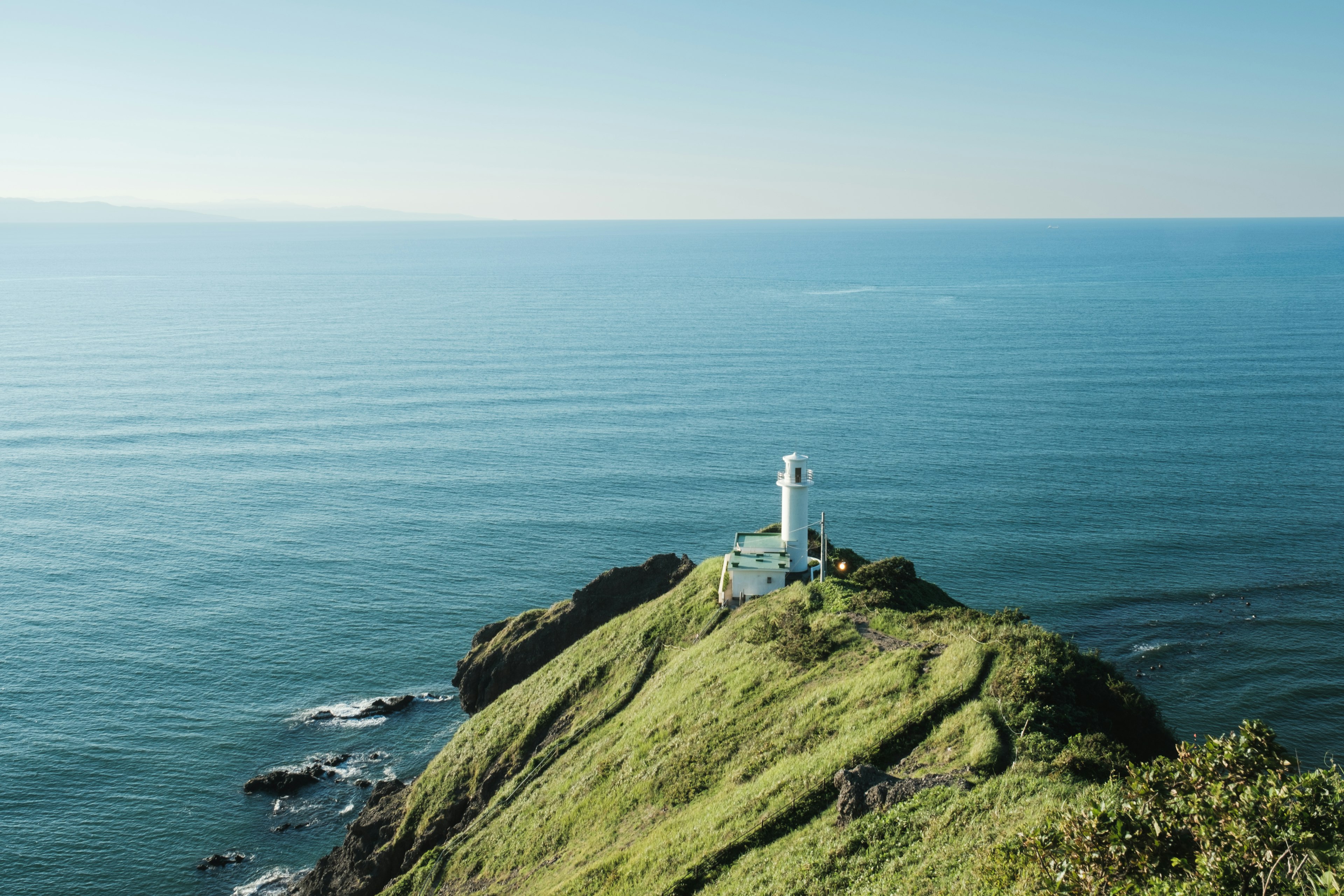 Un faro bianco su una collina verde circondato dall'oceano