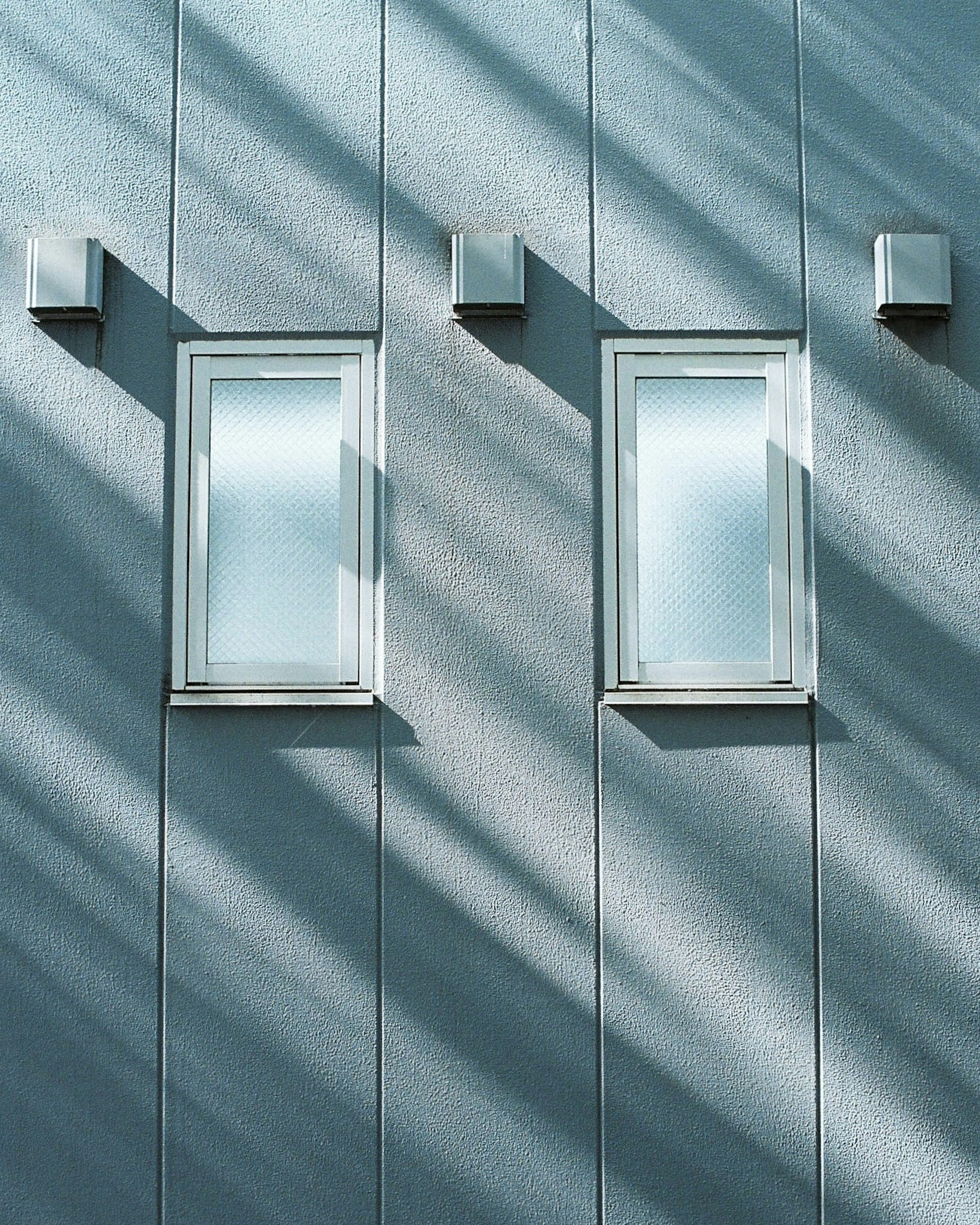 Deux fenêtres sur un mur bleu avec des ombres diagonales