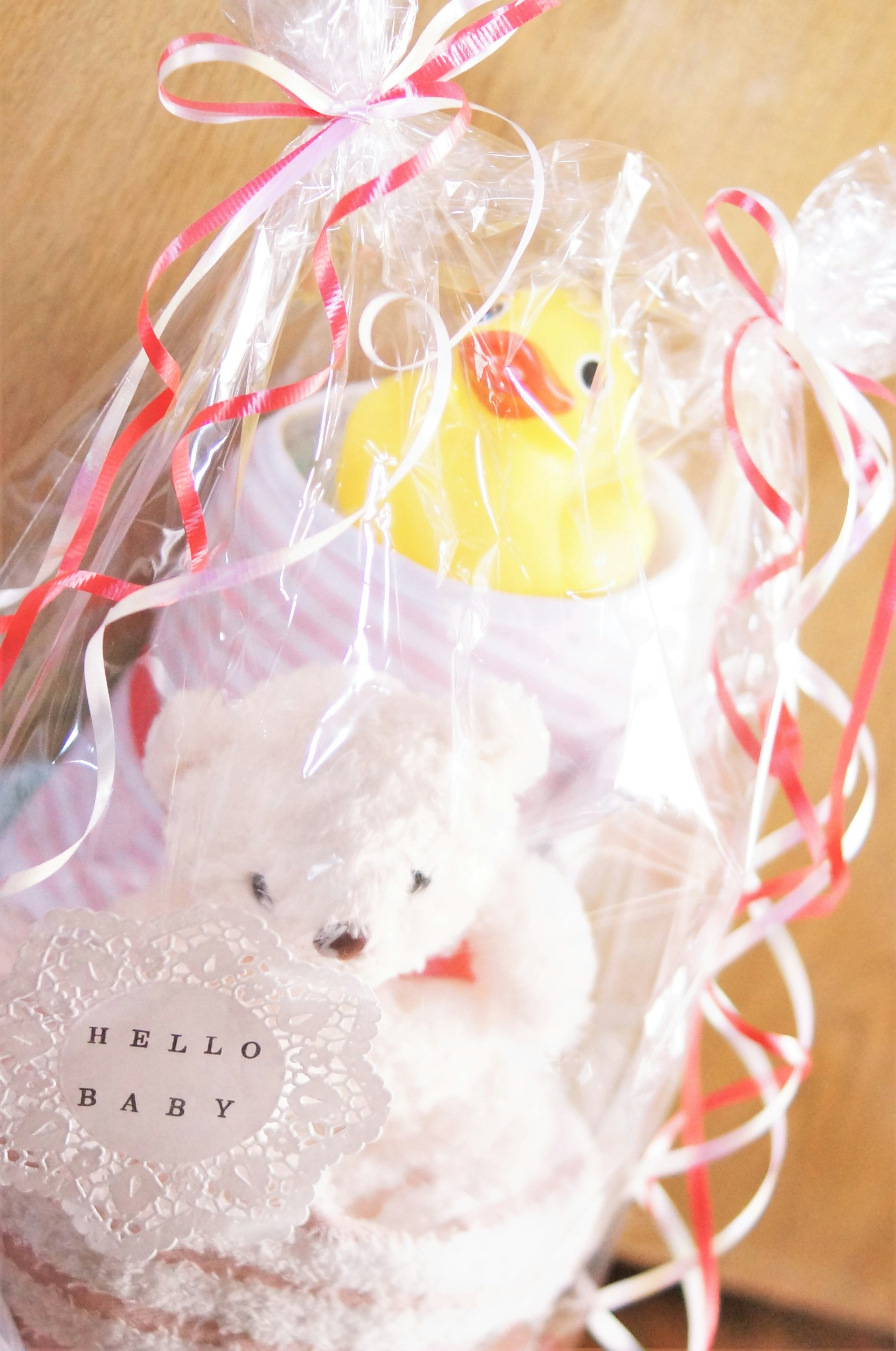 A gift box for a baby wrapped in red and white ribbons featuring a yellow duck and a white teddy bear