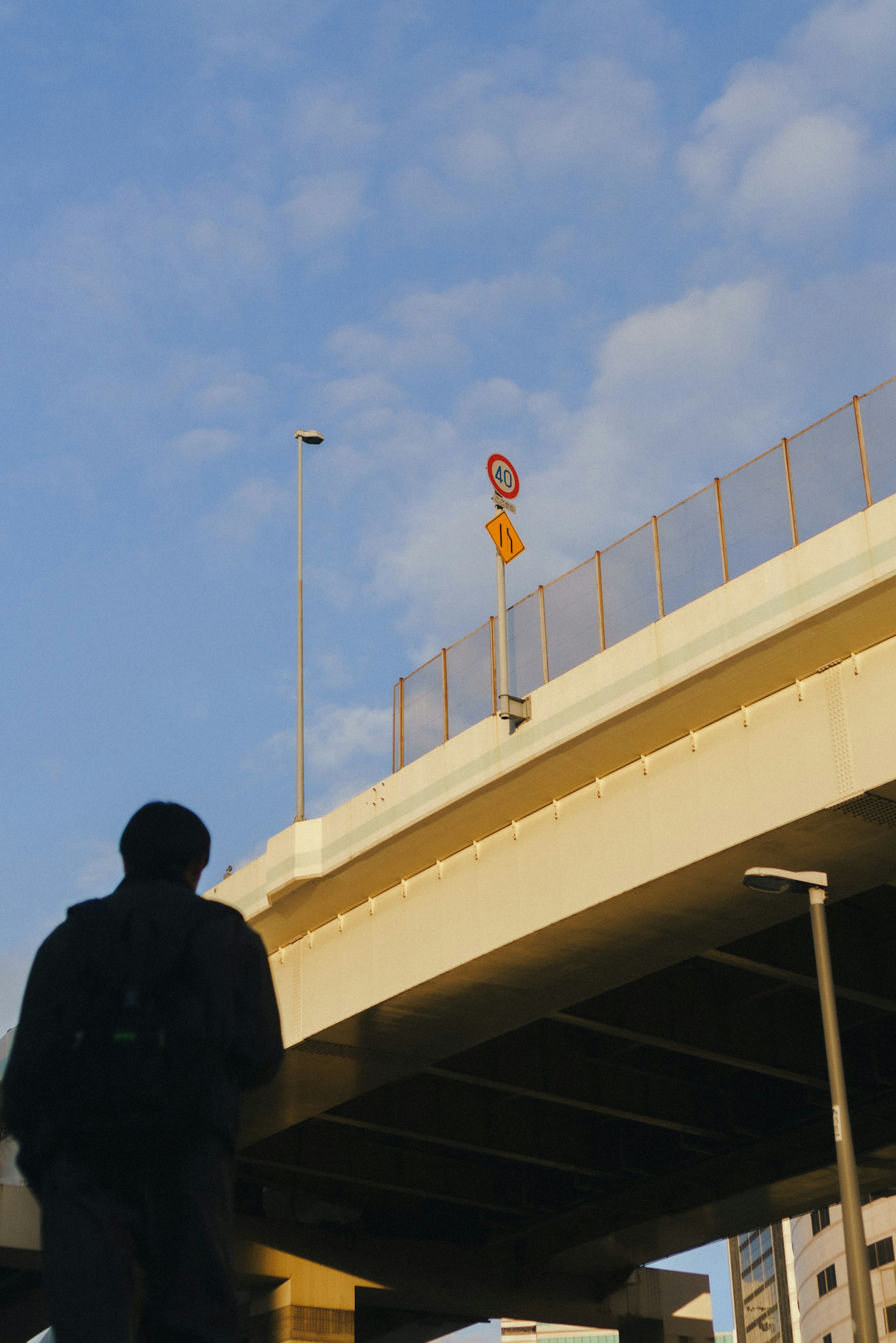 Silueta de una persona mirando hacia arriba desde debajo de un puente con cielo azul