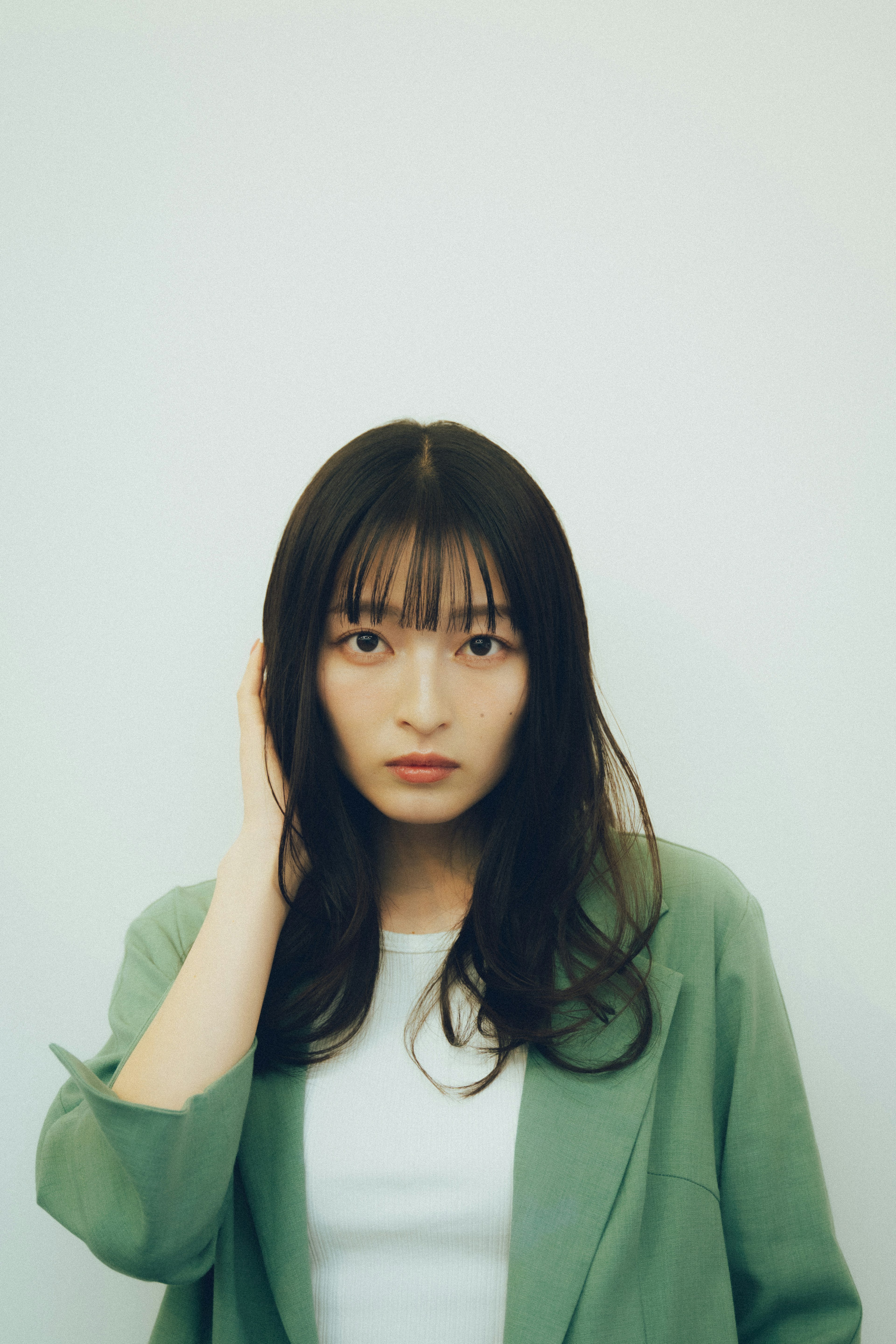 A woman in a green jacket looking at the camera while adjusting her bangs