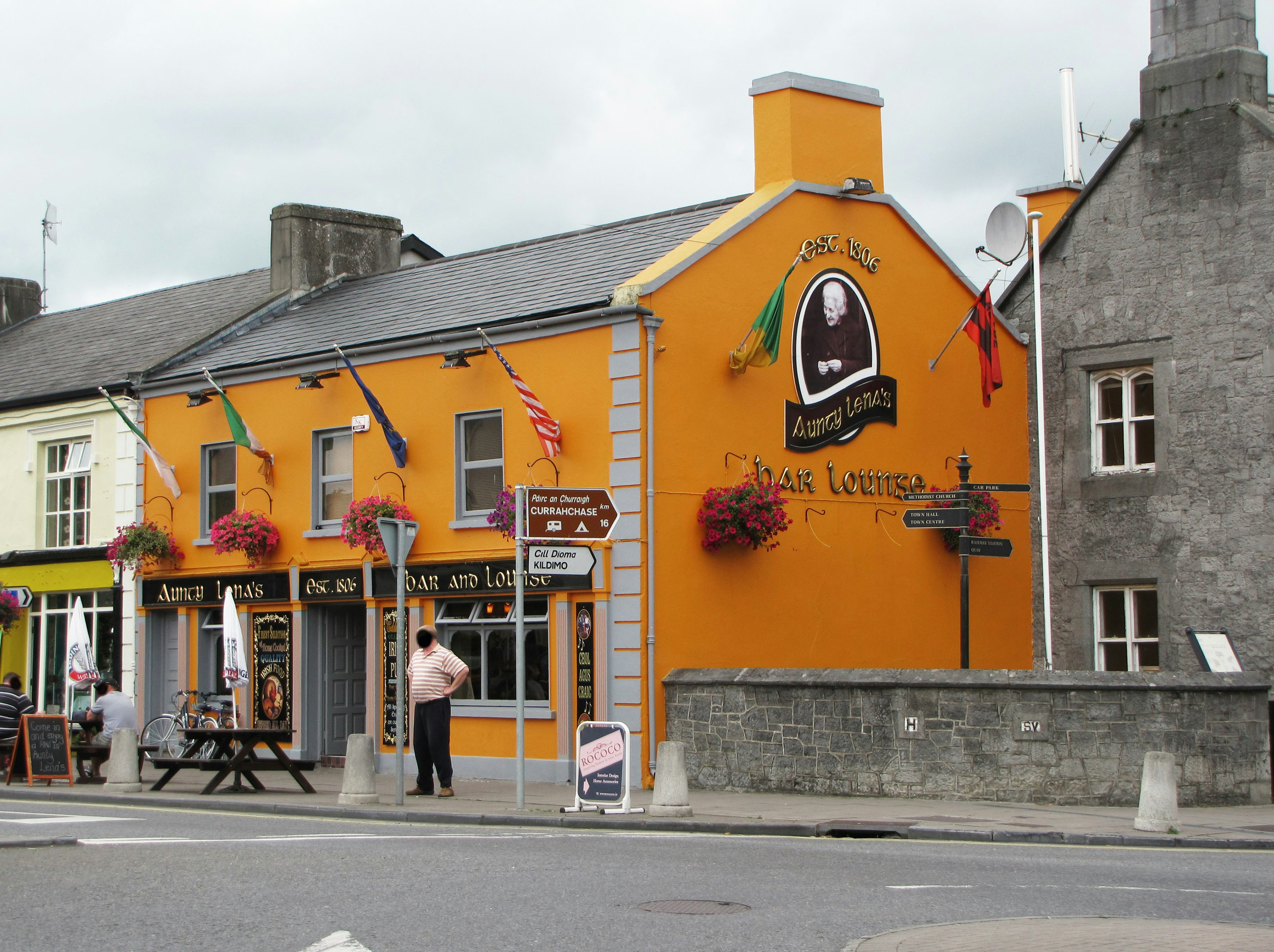 Street view featuring a vibrant orange pub and restaurant with hanging flower baskets