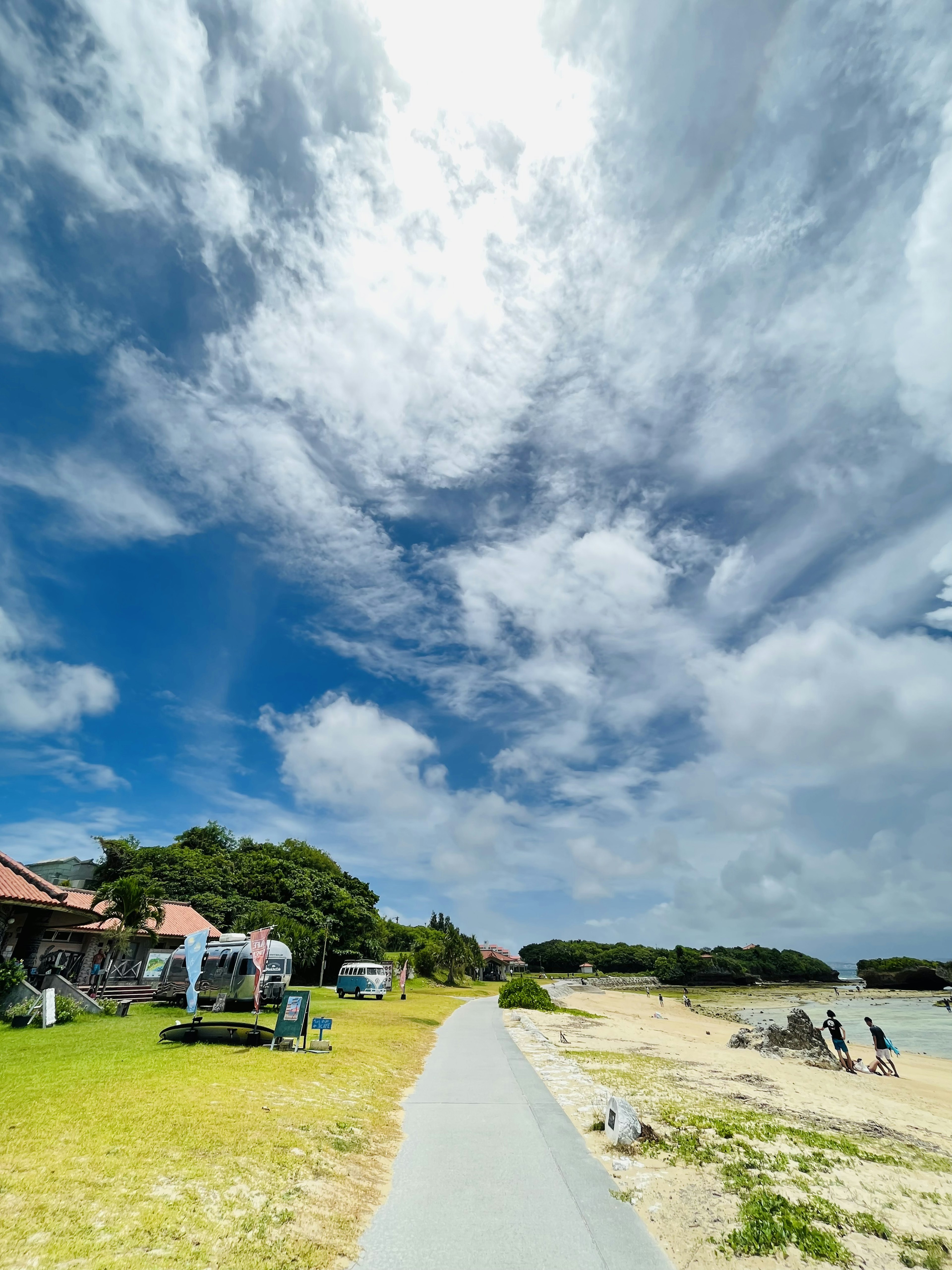 Vista escénica de la playa con cielo azul y nubes blancas Césped verde y camino pavimentado Personas disfrutando de la costa