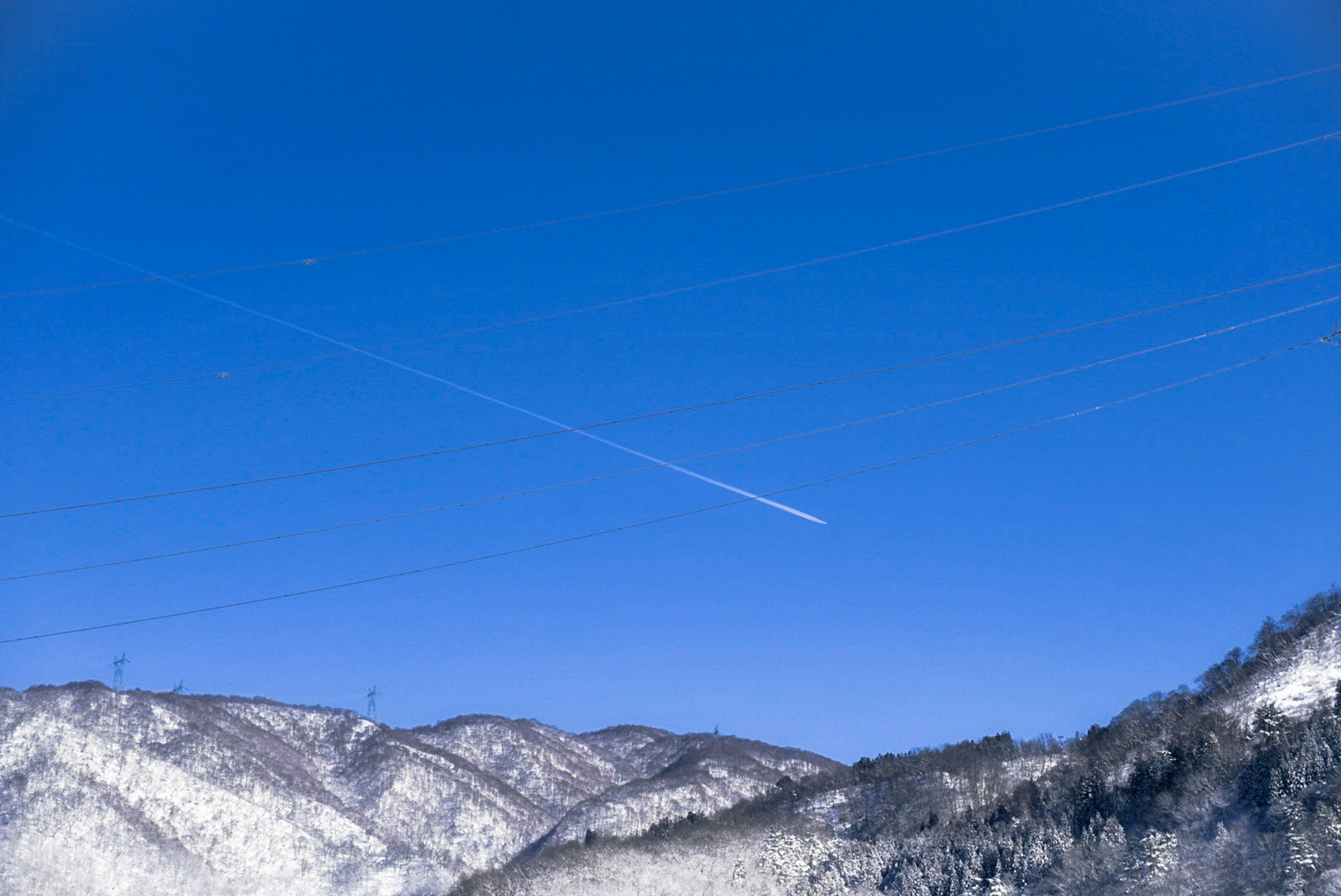 Un paesaggio di montagne innevate sotto un cielo blu con scie di aerei