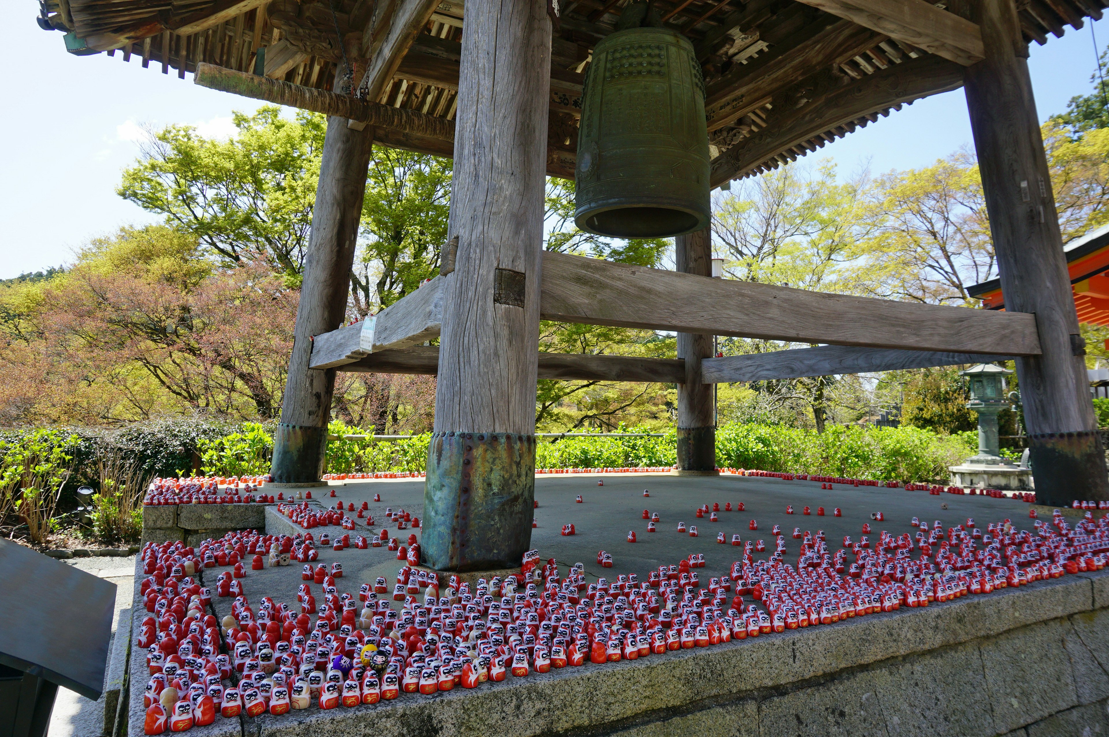 Tour de cloche en bois avec des figurines rouges disposées en dessous et une grande cloche