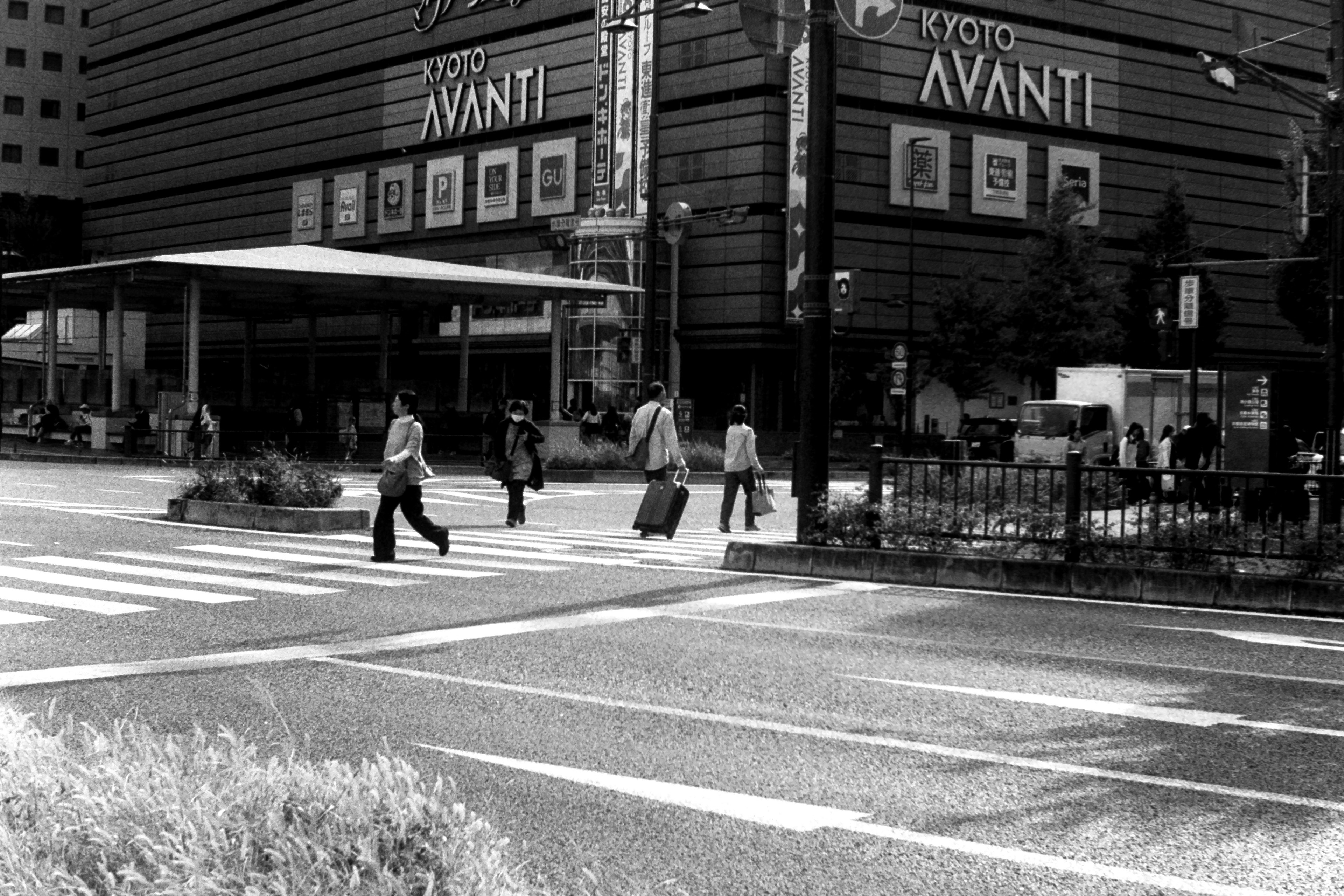 Scène de rue en noir et blanc avec un panneau AVANTI et des personnes traversant le passage piéton