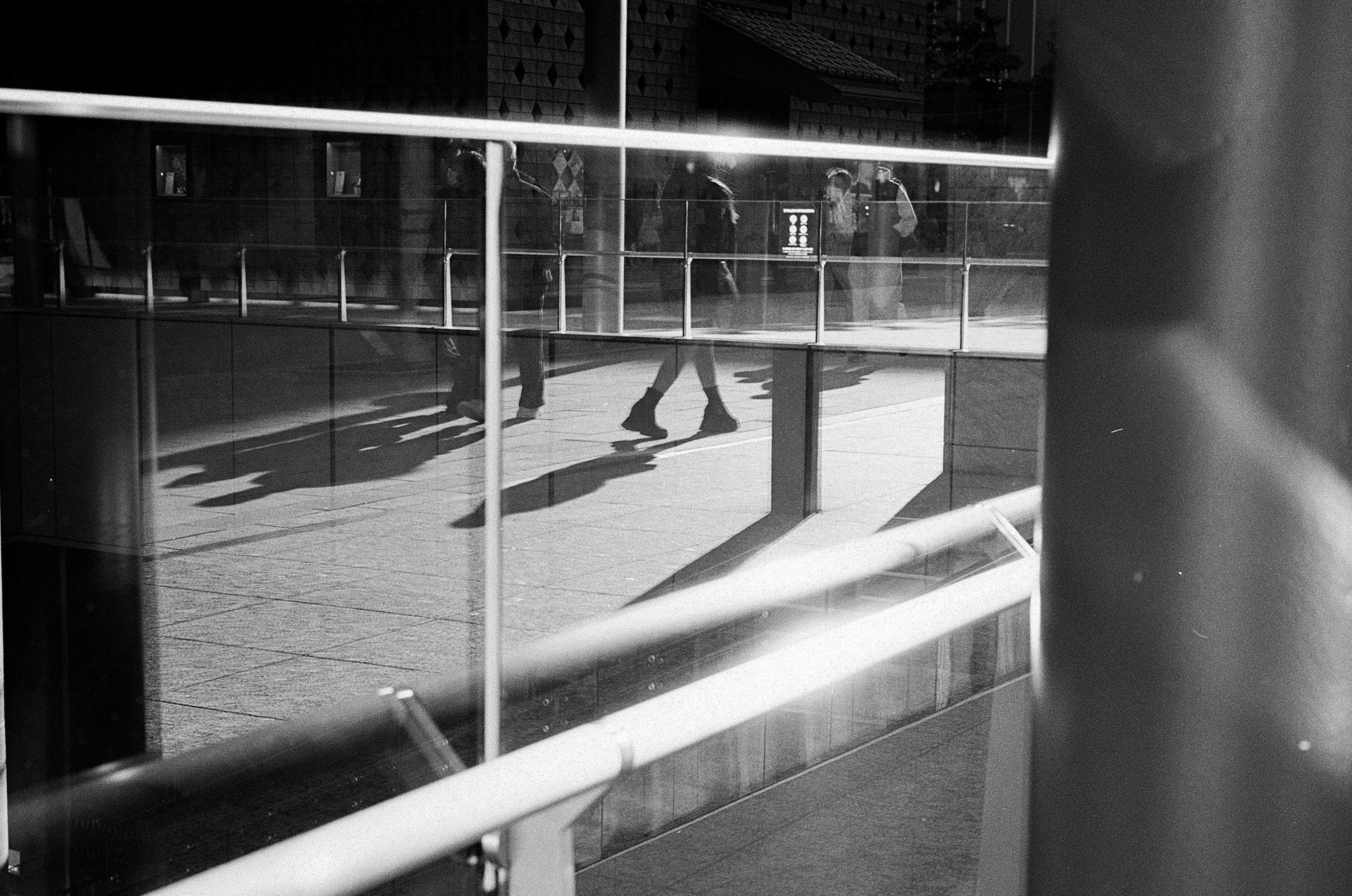 Black and white photo showing people walking through a glass railing