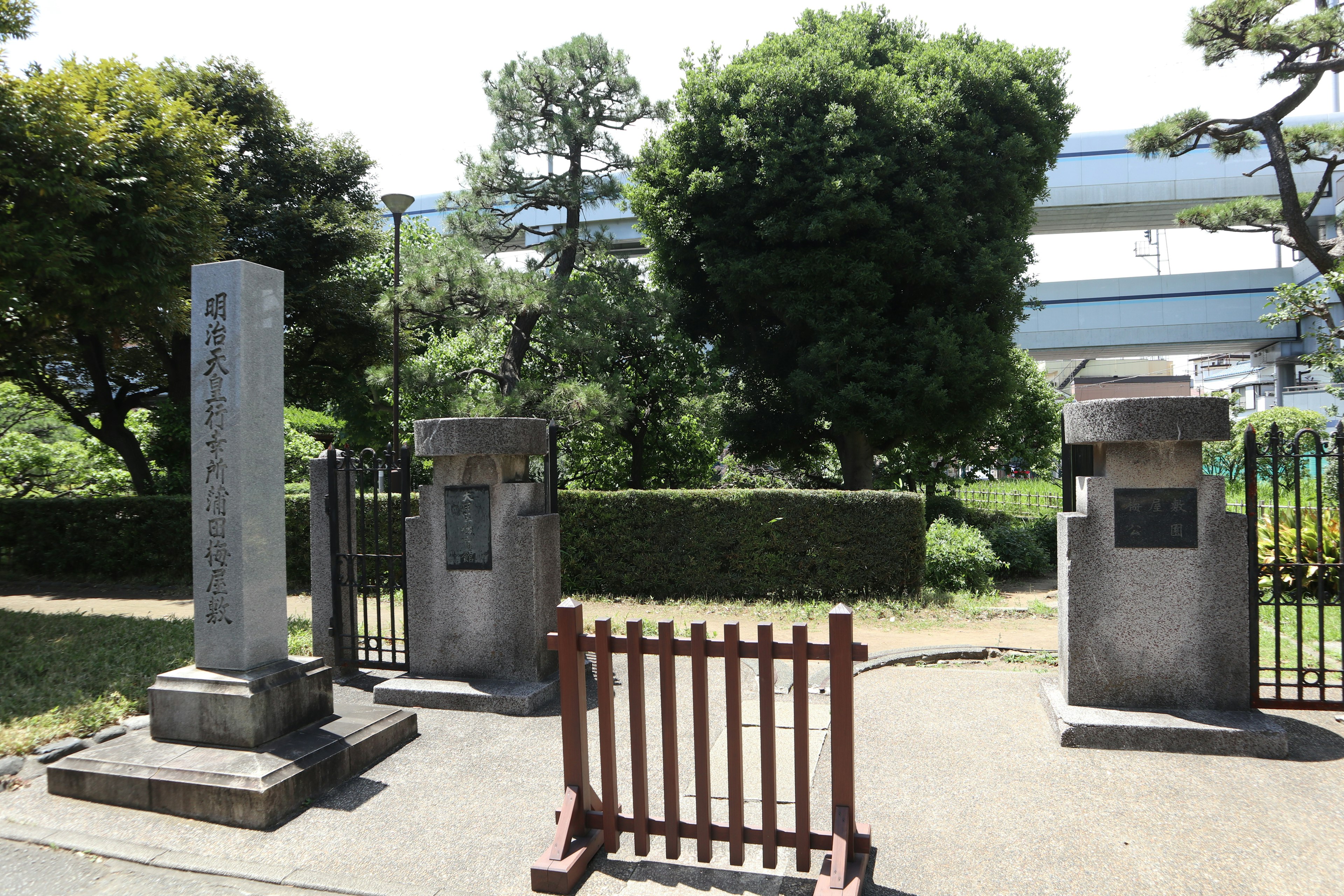 Pemandangan taman dengan monumen batu dan pagar kayu dikelilingi pohon hijau