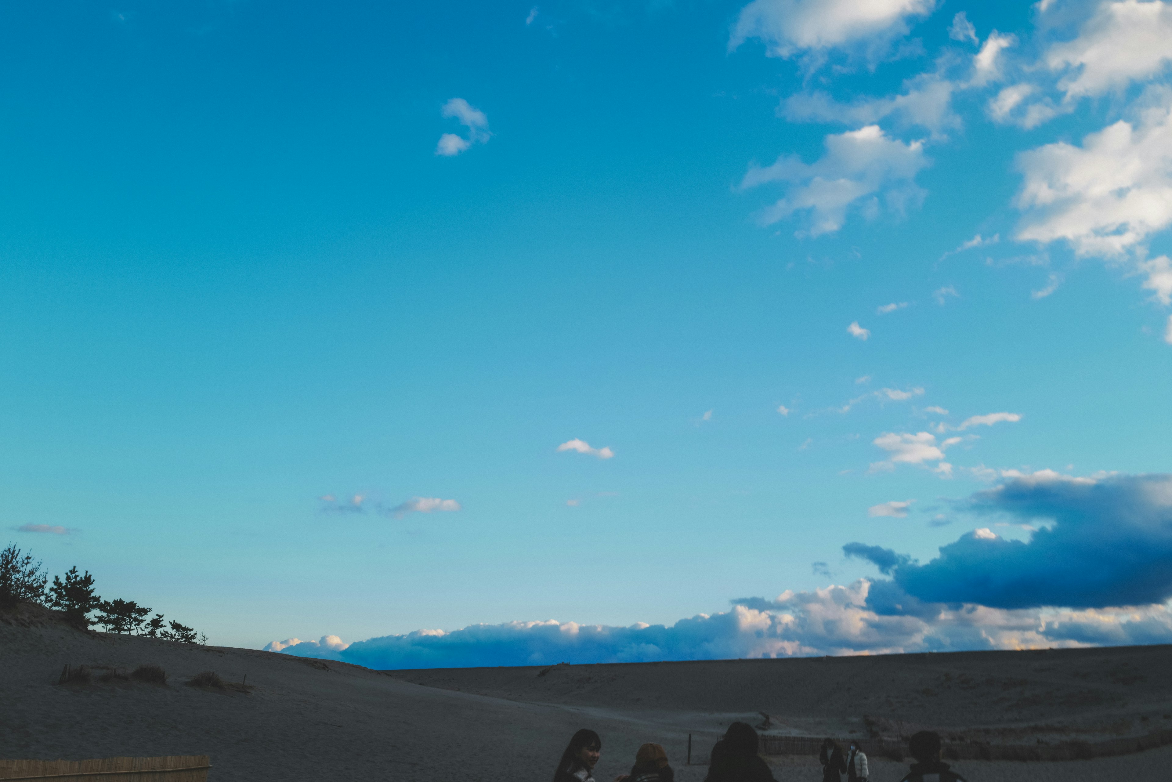 Dünenlandschaft unter einem blauen Himmel mit Wolken und Silhouetten von Menschen