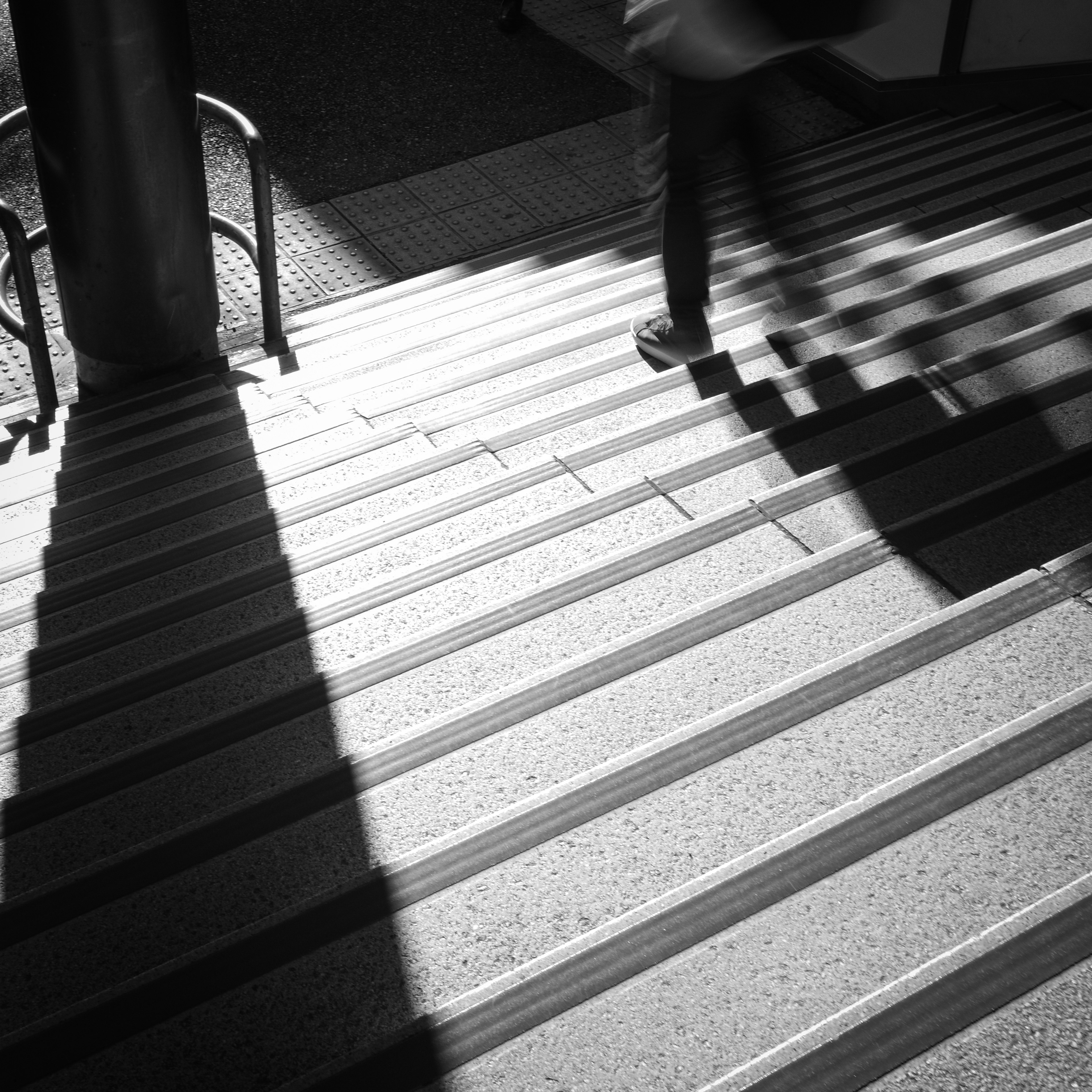 Persona bajando escaleras con fuerte contraste de sombras y luz