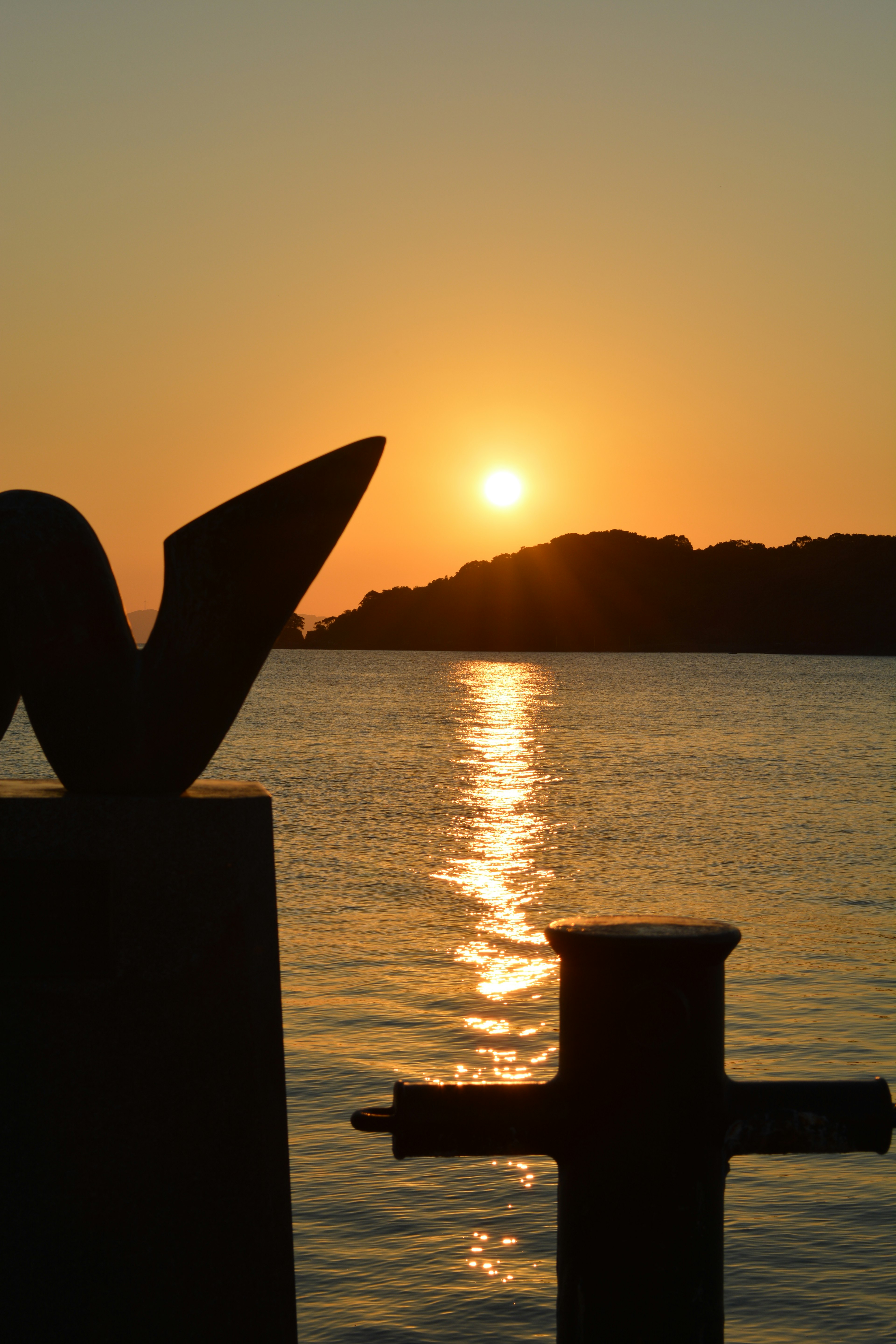 Sunset over the water with silhouetted island and sculptural objects in foreground