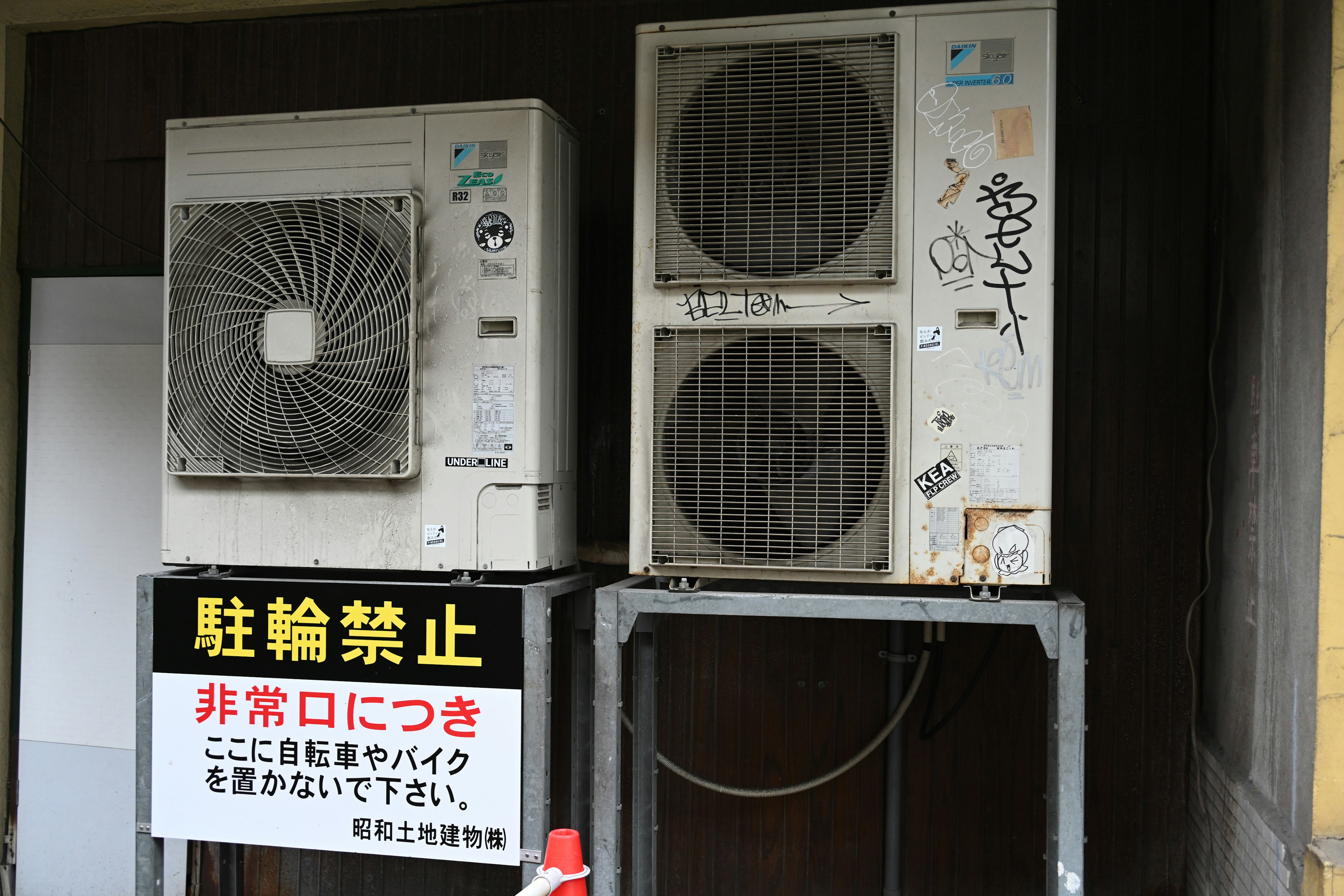 Two air conditioning units mounted on a wall with a no parking sign