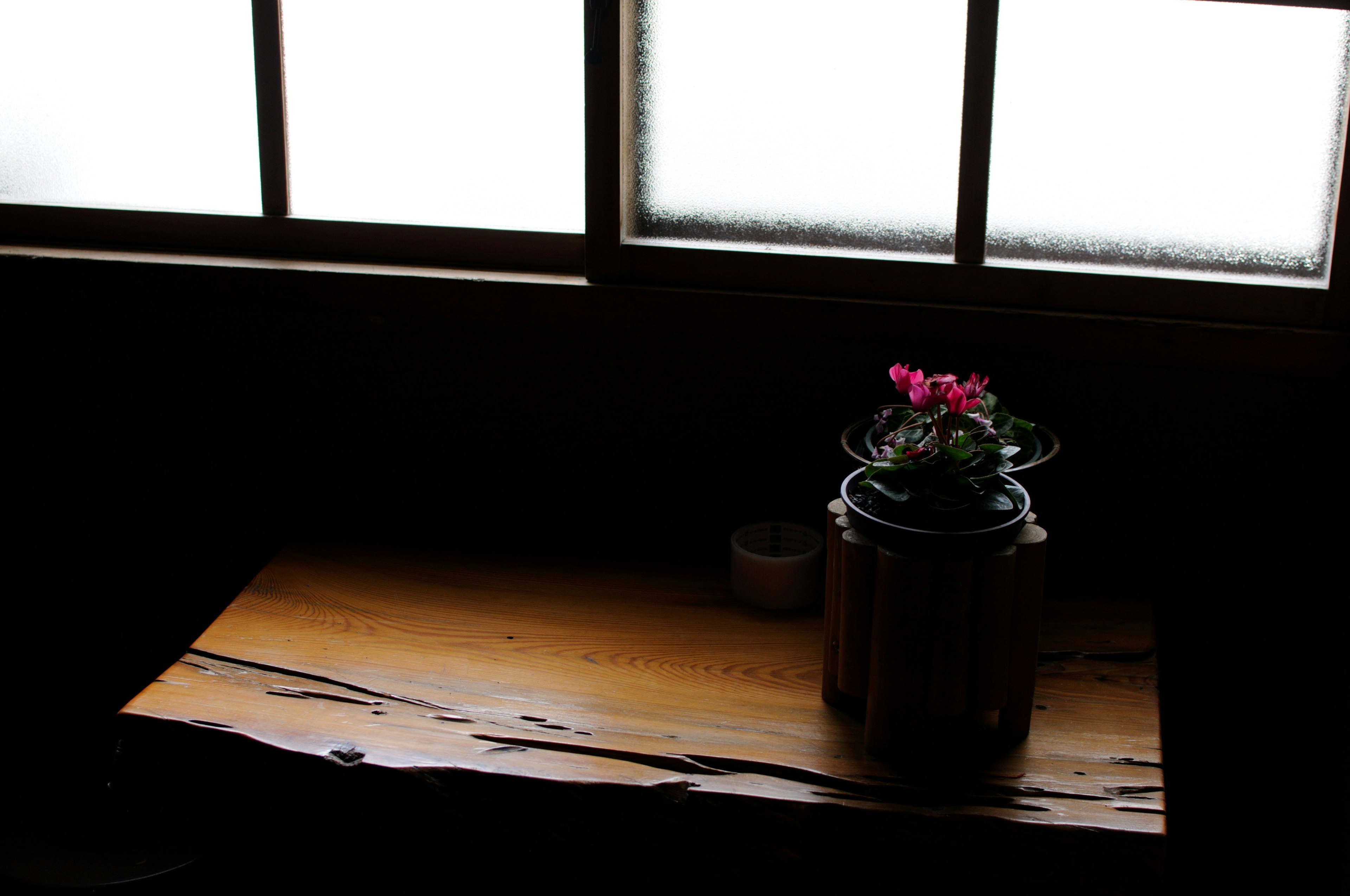 Una maceta con flores sobre una mesa de madera junto a la ventana