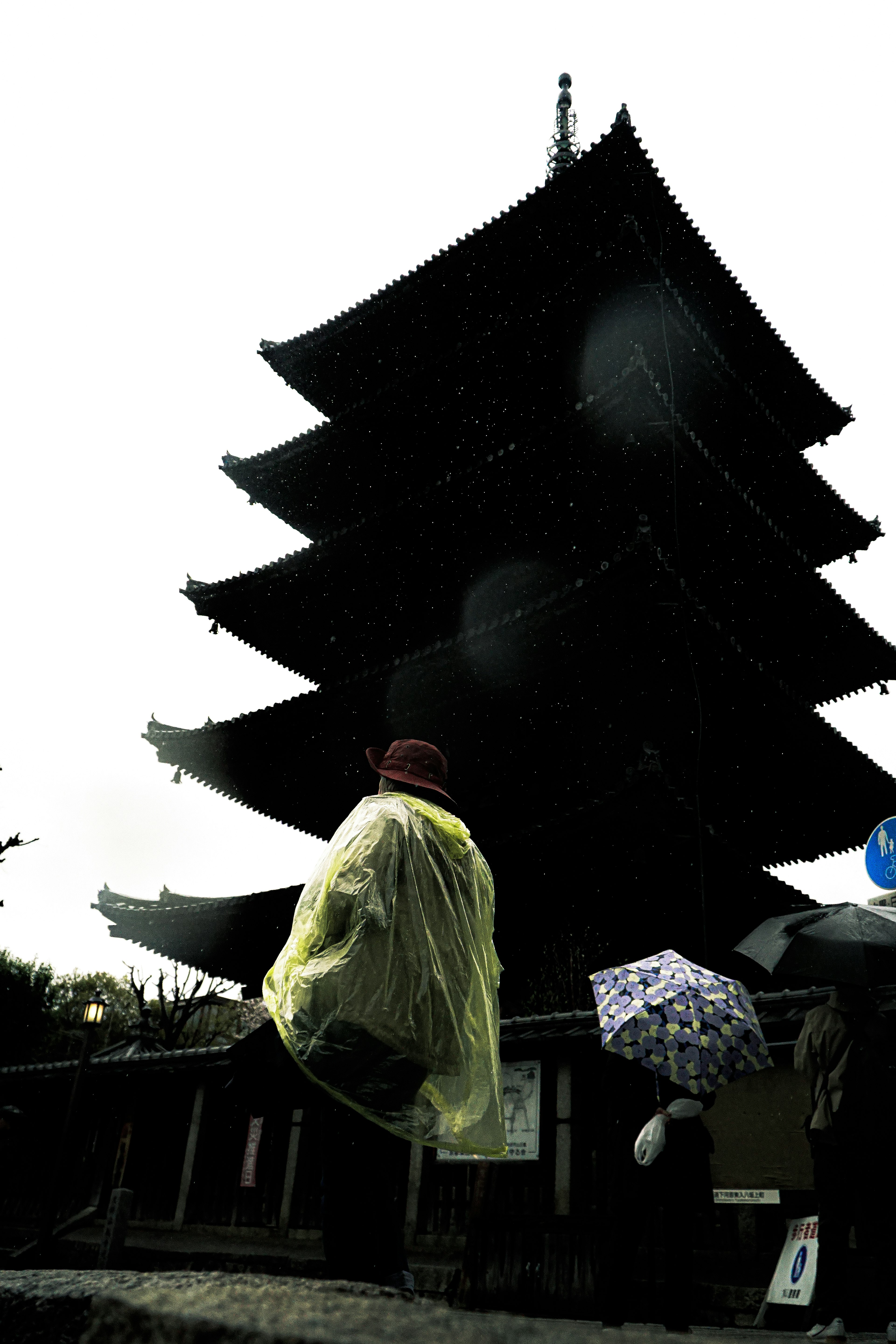 Una persona caminando bajo la lluvia con un paraguas frente a una pagoda de cinco pisos