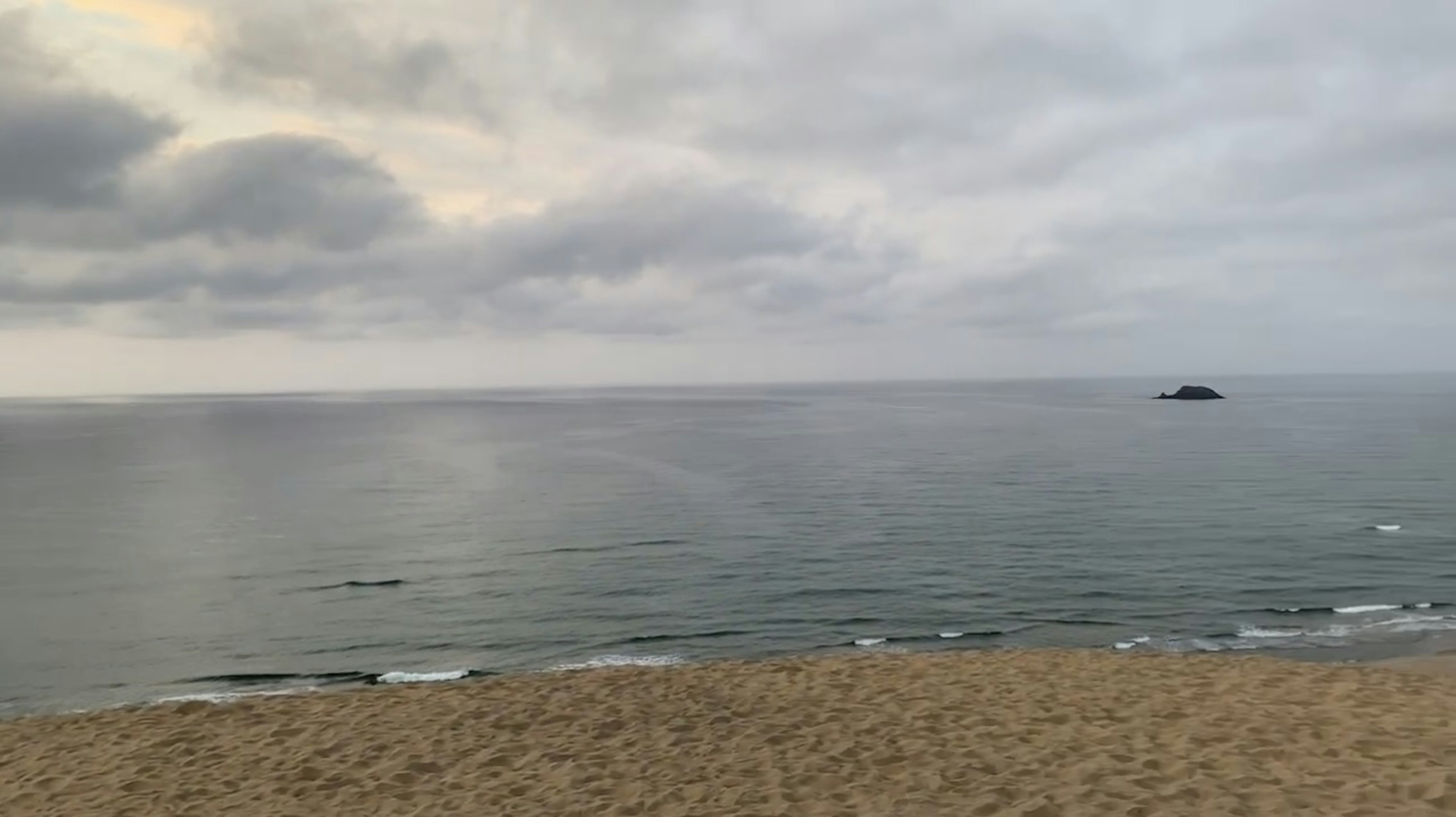 Pemandangan pantai dengan langit mendung dan gelombang tenang