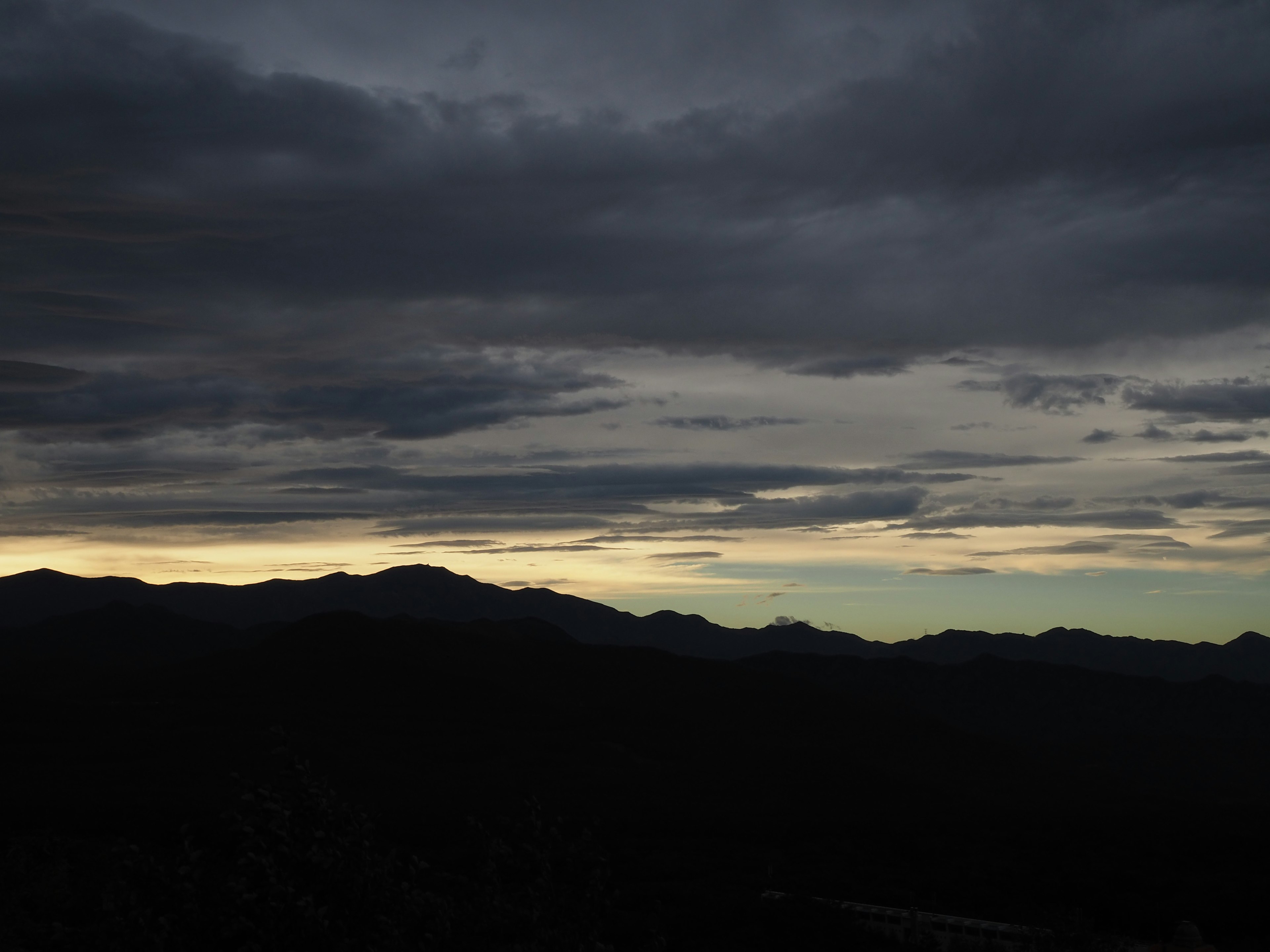 暗い雲に覆われた山々のシルエットと薄明かりの空