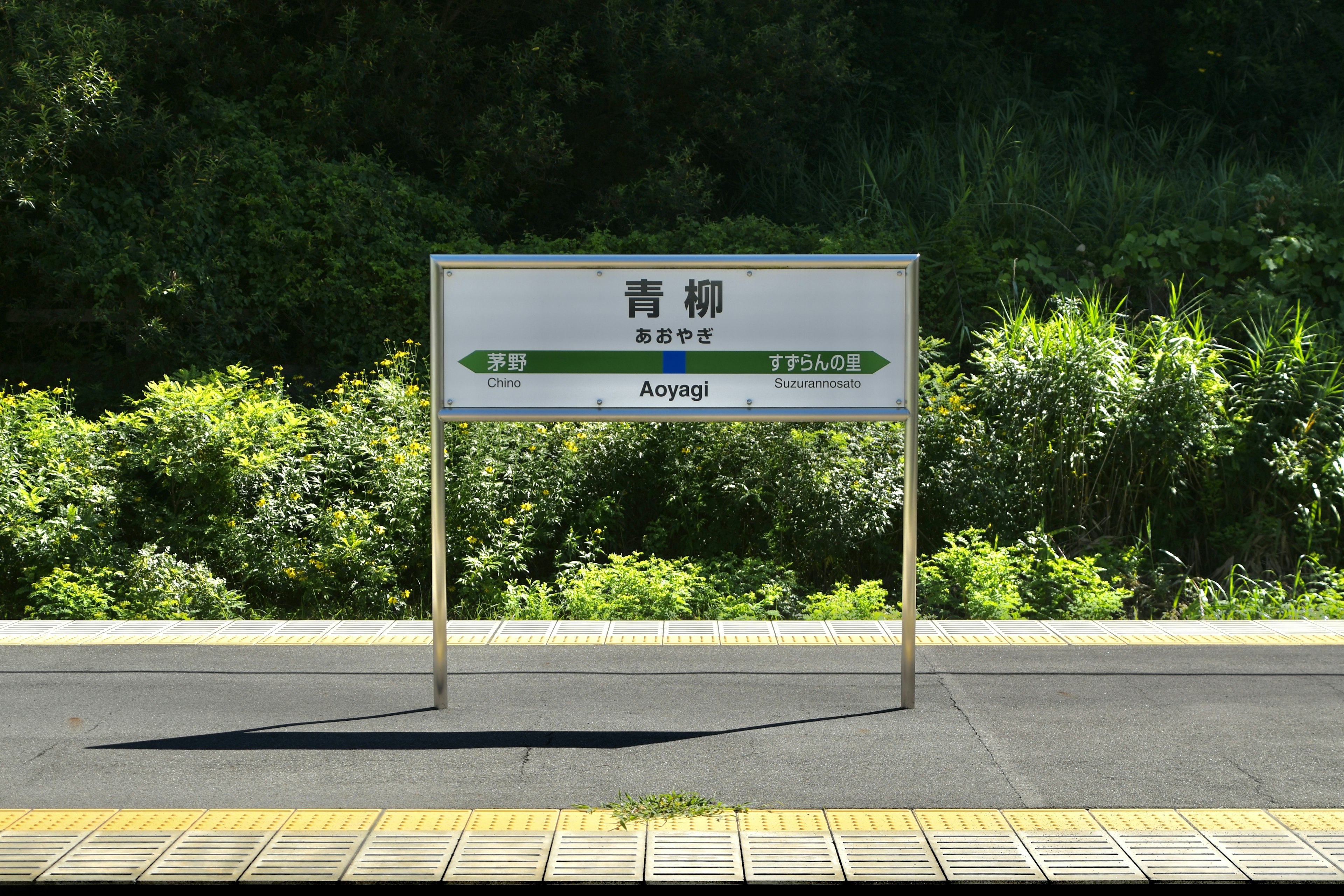 Schild der Station Aome mit grünen Pflanzen im Hintergrund