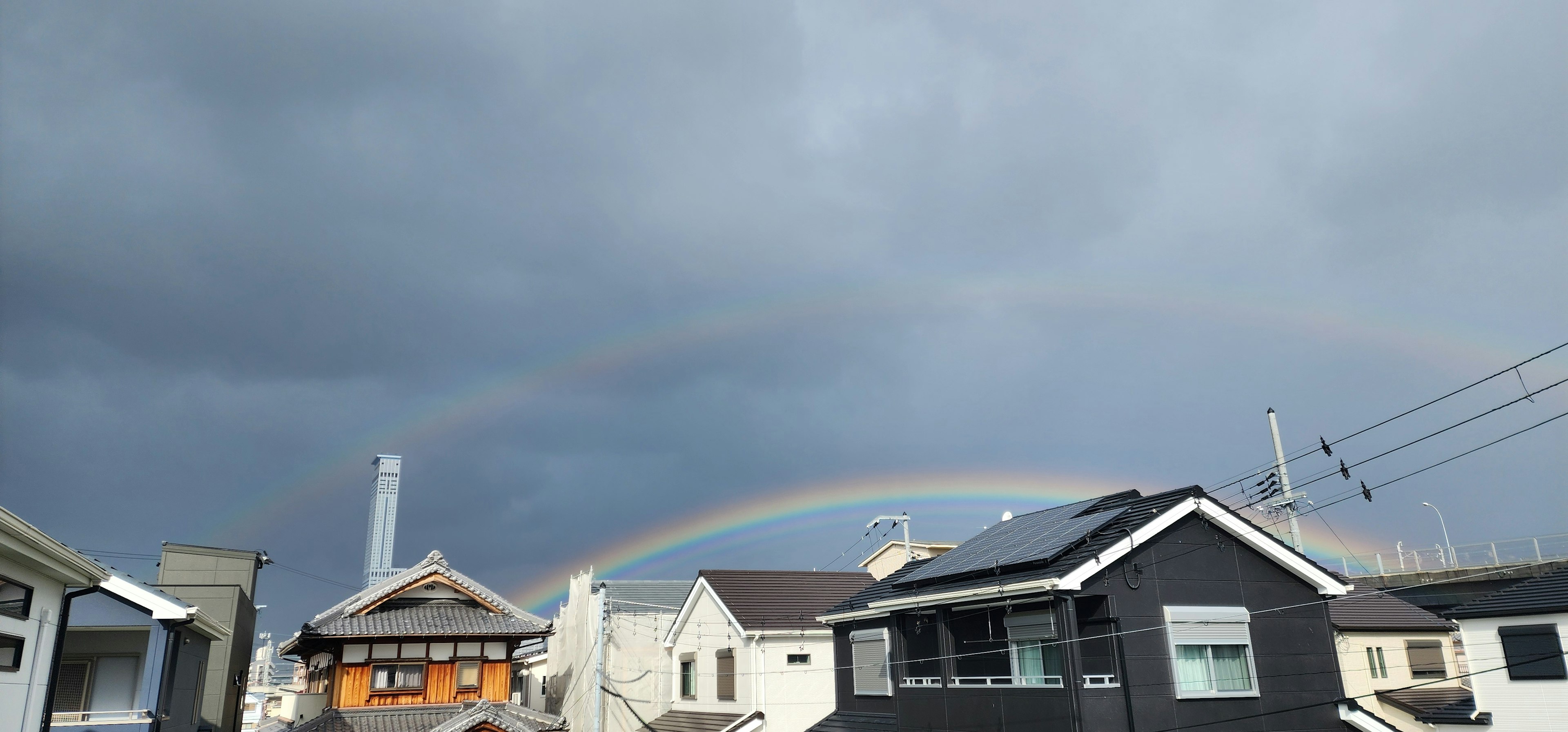 Double rainbow arching over a residential area under dark clouds