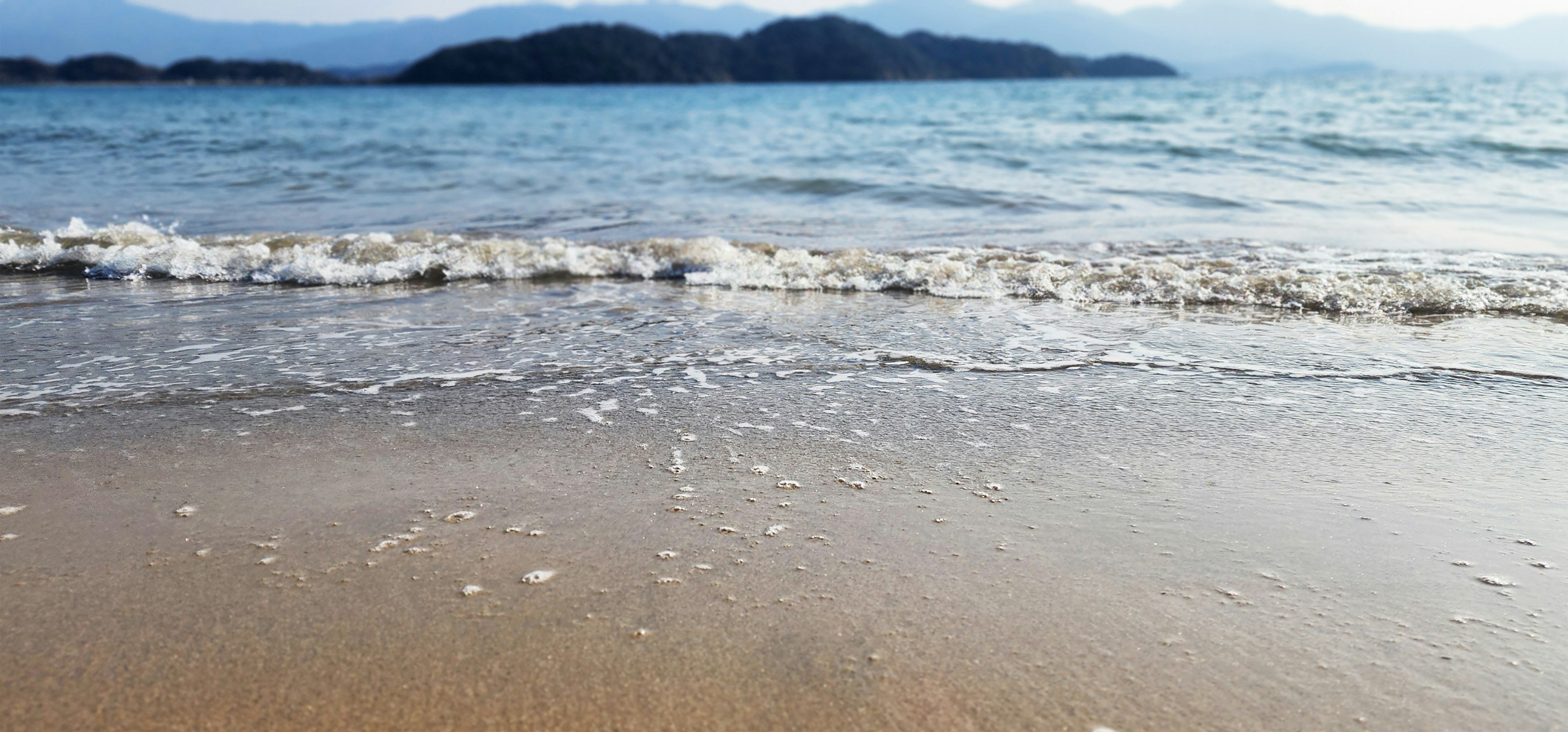 Pemandangan pantai berpasir dengan lautan biru dan pulau-pulau di kejauhan