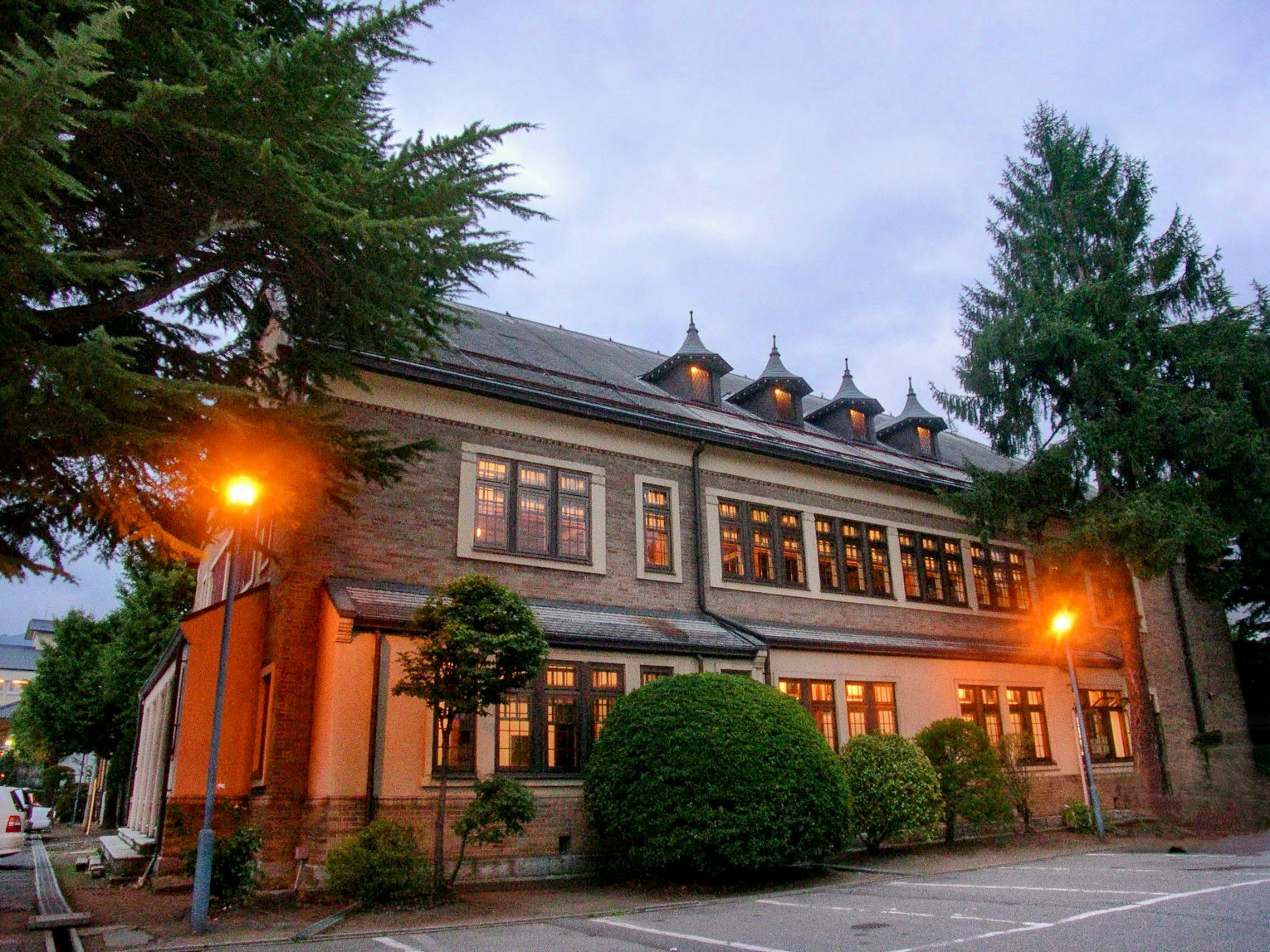 Exterior of an old building at dusk surrounded by green trees and streetlights